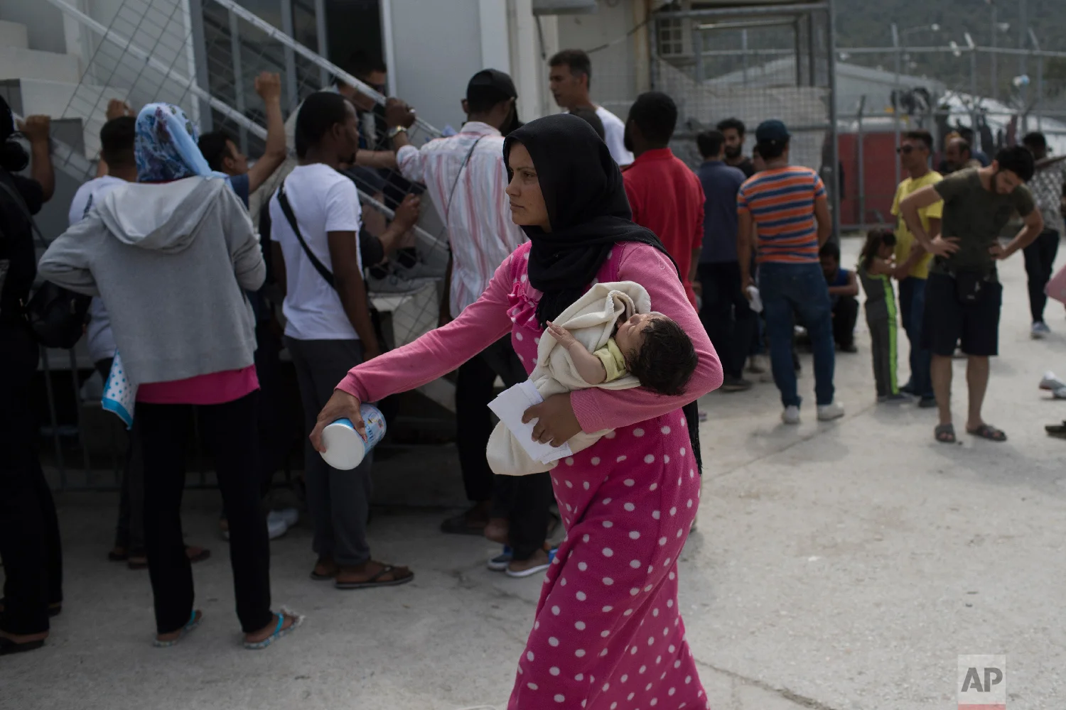 A woman walks with her baby as migrants and refugees wait outside UNHCR offices for their papers inside the camp of Moria on Lesbos, Greece on Friday, May 4, 2018. (AP Photo/Petros Giannakouris)