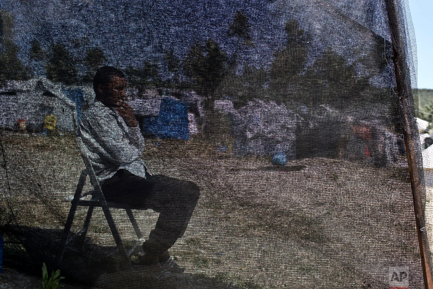 Hasan, no other name given, from Deir ez-Zor in Syria, who arrived in Greece six months ago, sits behind the net of his tent at a makeshift camp outside the official camp of Moria at the island of Lesbos on Wednesday, May 2, 2018. (AP Photo/Petros Giannakouris)