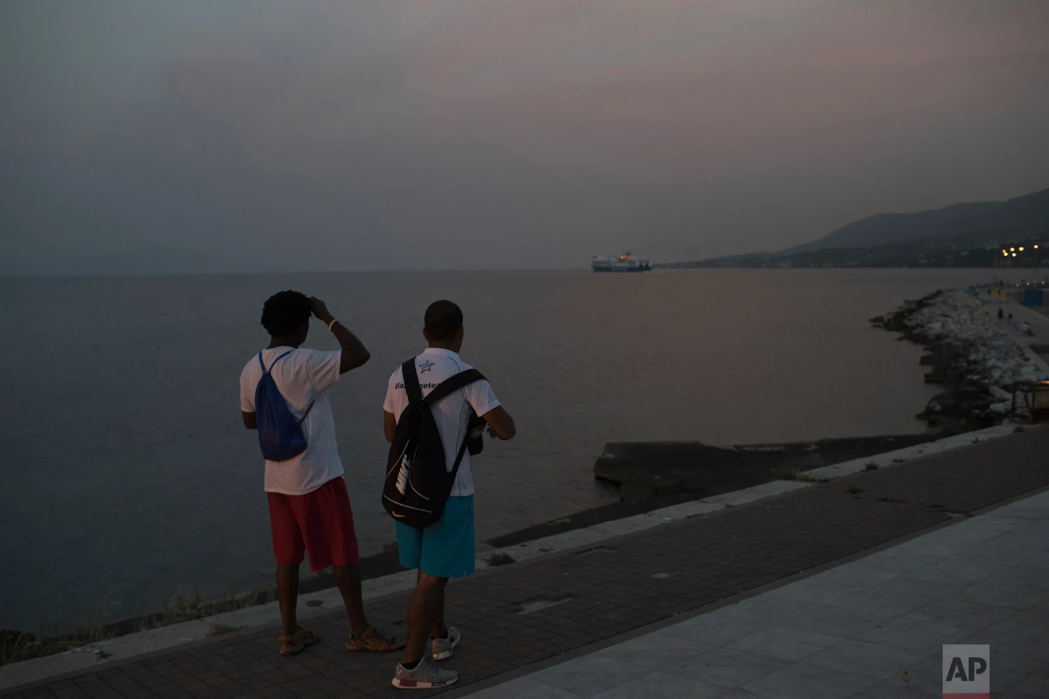 Two men watch the ferry leaving the port of Mytilene on the northeastern Aegean island of Lesbos, Greece on Thursday, May 4, 2018. (AP Photo/Petros Giannakouris)