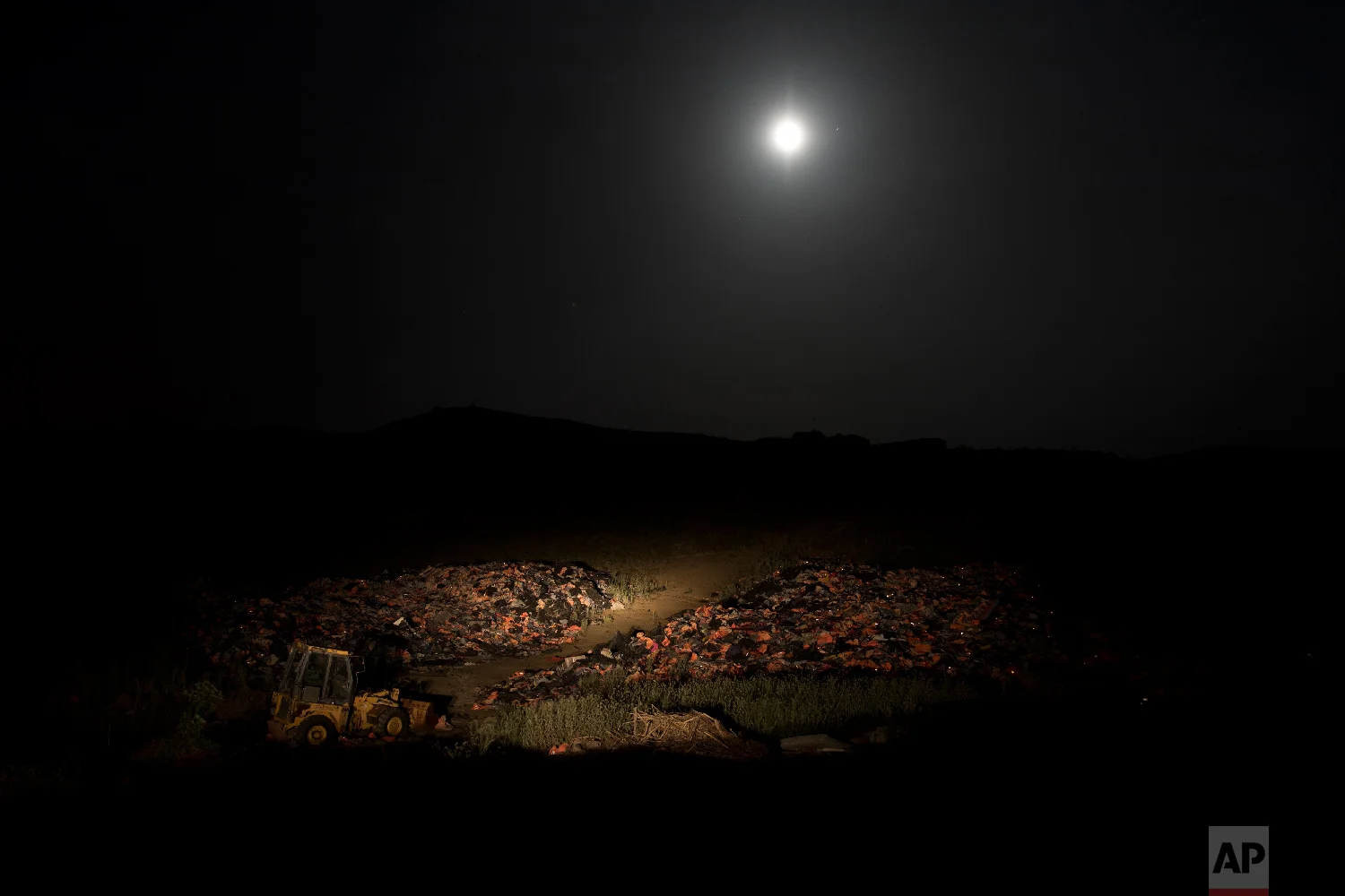 The moon rises above a huge pile of discarded life vests and dinghies used by migrants and refugees crossing from the nearby Turkish coast, at a dump on the island of Lesbos on Saturday, May 5, 2018. (AP Photo/Petros Giannakouris)