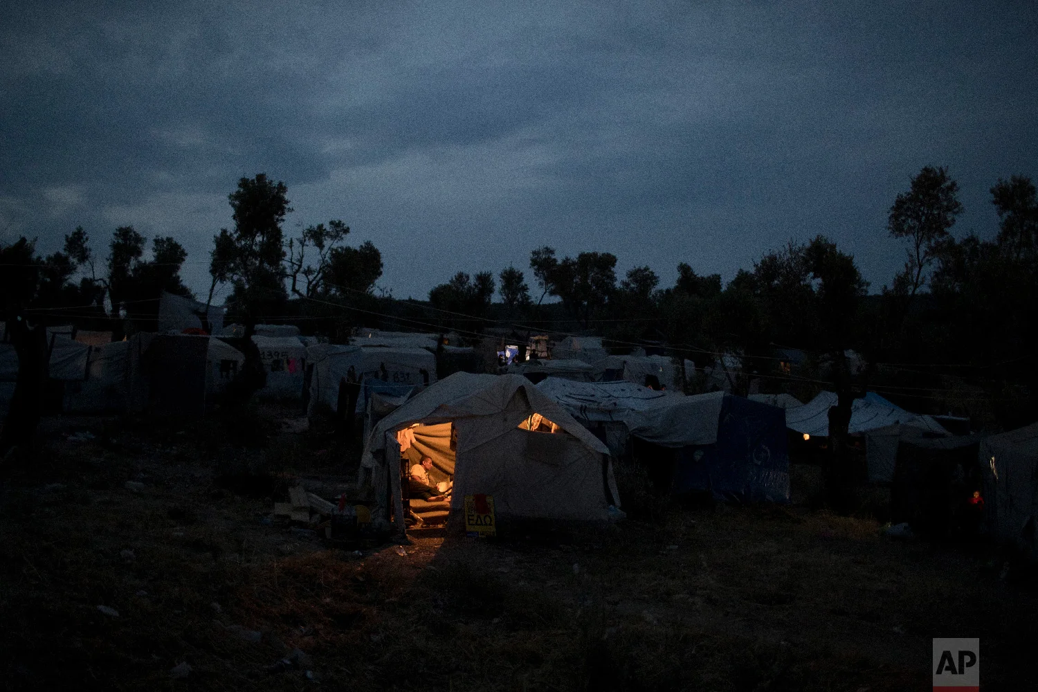 A Syrian man reads inside his tent at a makeshift camp outside Moria on the northeastern Aegean island of Lesbos, Greece on Saturday, May 5, 2018. (AP Photo/Petros Giannakouris)