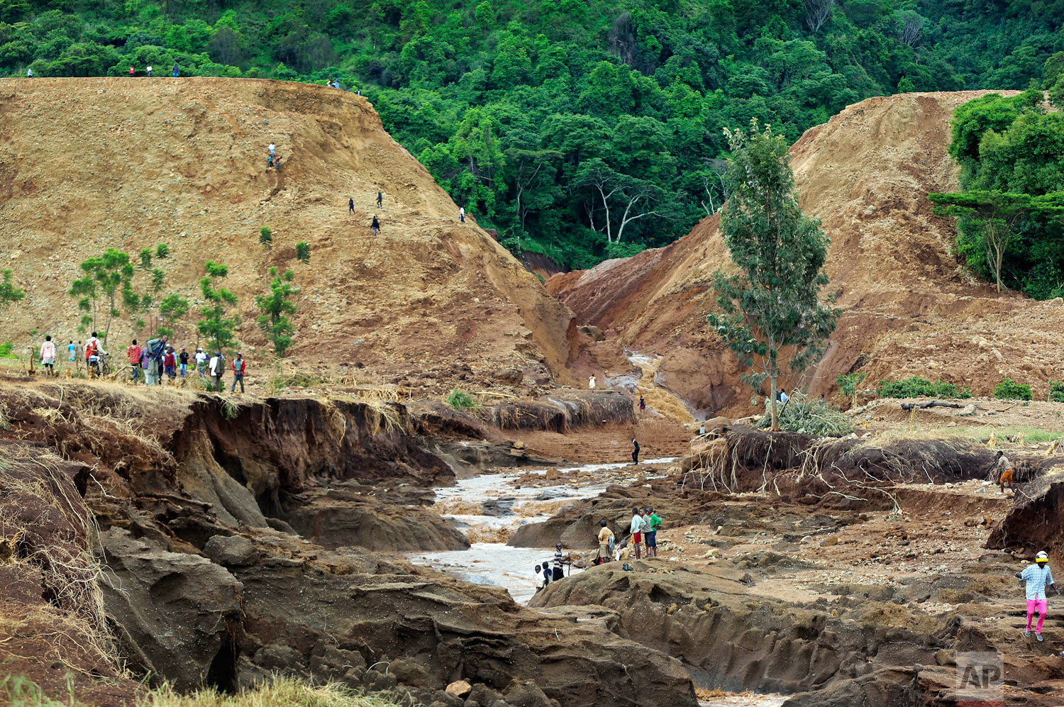 People gather in front of the broken banks of the Patel Dam near Solai in Kenya's Rift Valley, Thursday, May 10, 2018. The dam burst killing at dozens and forcing hundreds from their homes, officials said Thursday. At least 20 of the dead were children, police said. It was the deadliest single incident yet in the seasonal rains that have killed more than 170 people in Kenya since March. The floods hit as the East African nation was recovering from a severe drought that affected half of the country. (AP Photo)