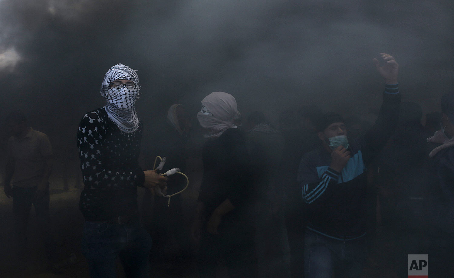 Palestinian protesters hurl stones at Israeli troops while engulfed in smoke from burning tires near the Gaza Strip's border with Israel, east of Khan Younis, in the Gaza Strip, Monday, May 14, 2018. (AP Photo/Adel Hana)