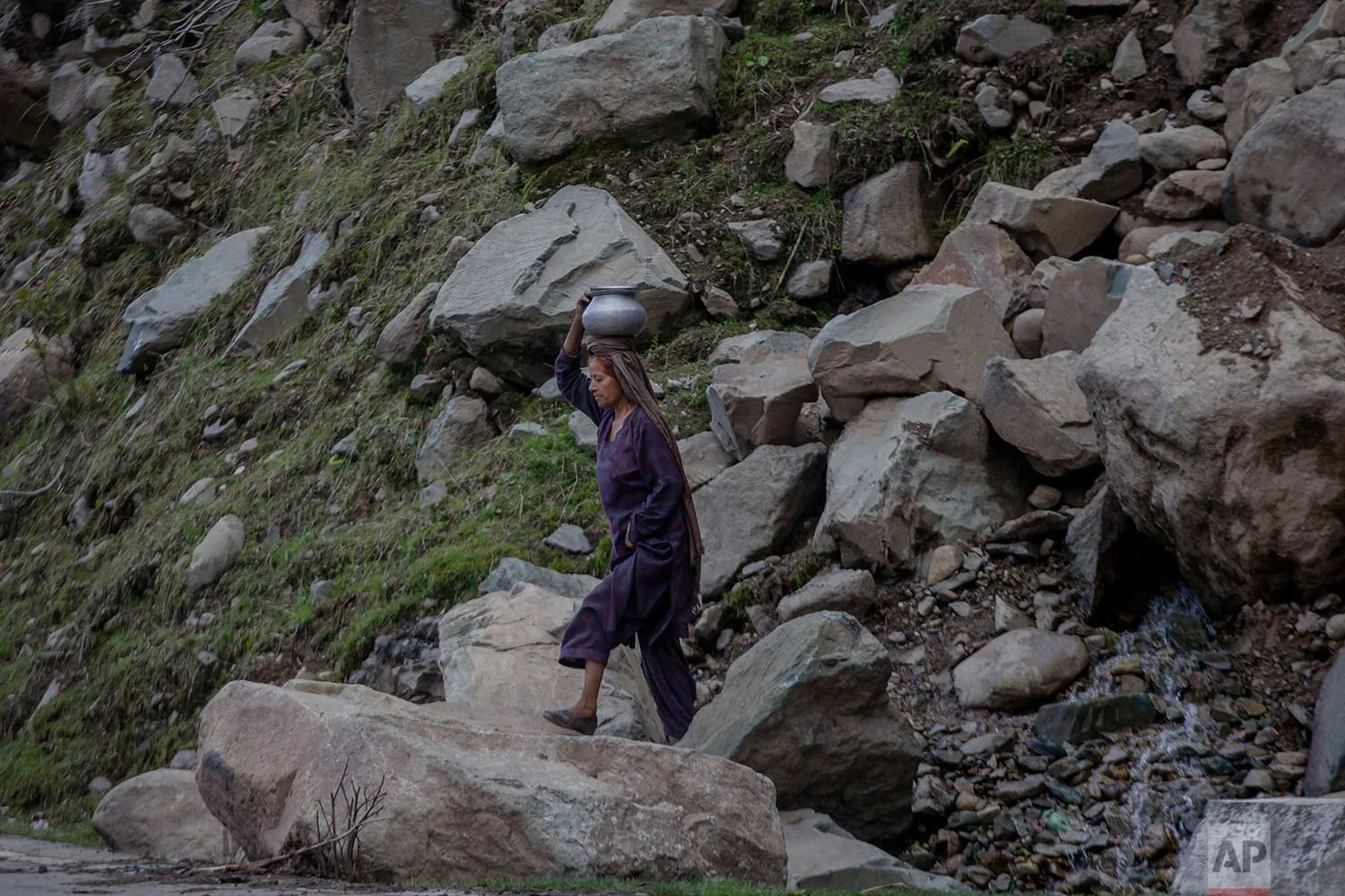 In this May 9, 2018, photo, a Kashmiri nomadic Bakarwal woman carries water after collecting it from a waterfall in Dubgan, 70 kilometers (43 miles) south of Srinagar, Indian controlled Kashmir. (AP Photo/Dar Yasin)