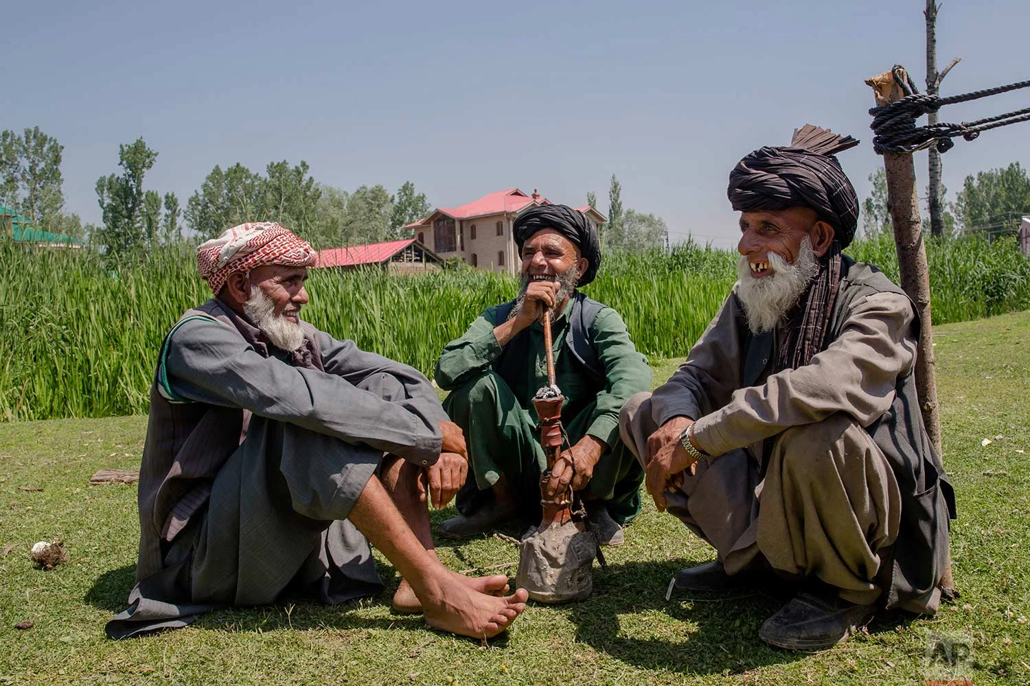 In this May 11, 2018, photo, photo, elderly Kashmiri nomadic Bakarwal men share a lighter moment as they smoke a hubble bubble or Hukka near a camp, outskirts of Srinagar, Indian controlled Kashmir. (AP Photo/Dar Yasin)
