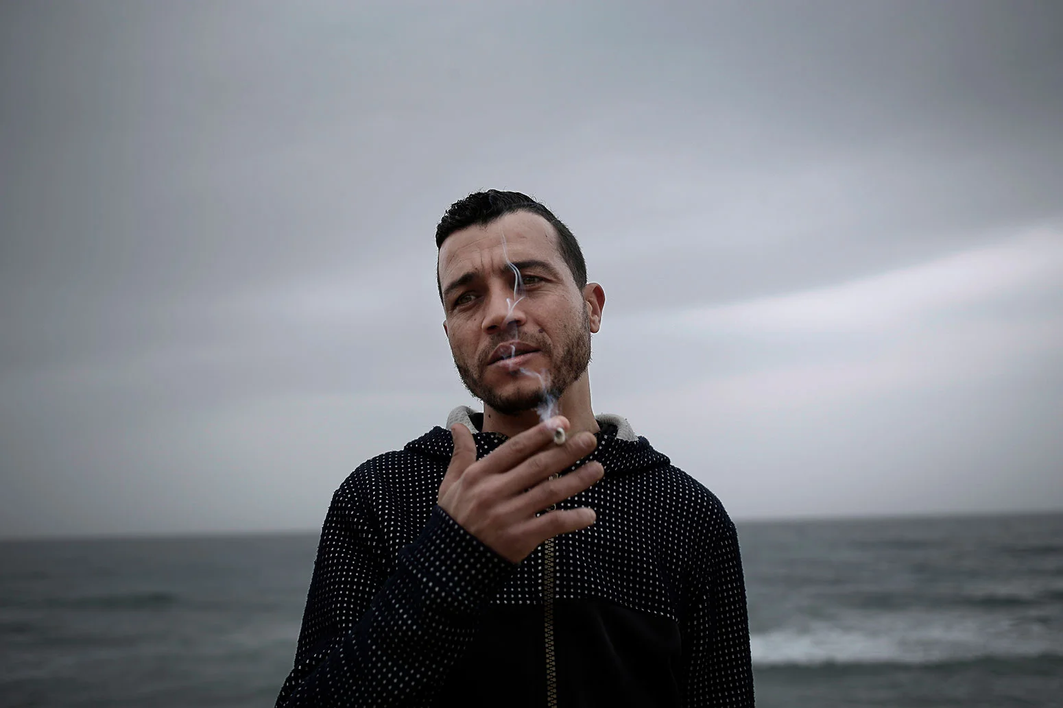 In this Saturday, April 14, 2019 photo, Ahmed Ayouby, 32, smokes a cigarette at the beach where migrants leave for Italy, in Ras Jebel, Tunisia. (AP Photo/Nariman El-Mofty)