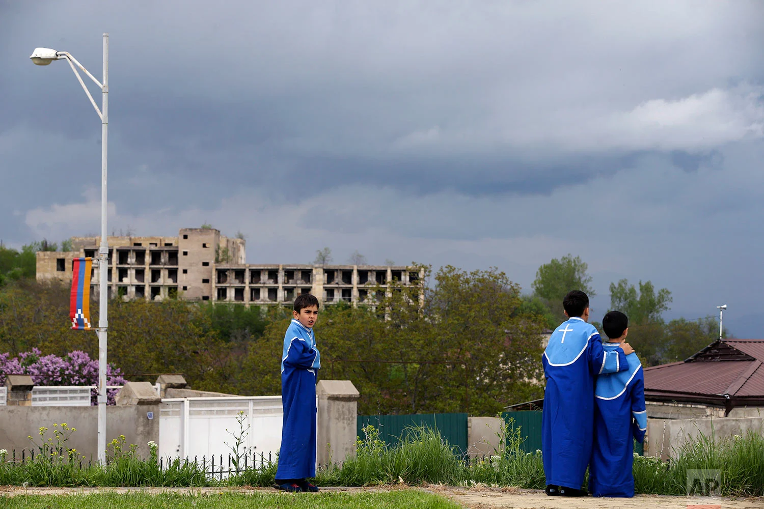 In this Thursday, May 10, 2018, children stand at the yard of a church as a destroyed building during the war is seen in the background in Shusha town. (AP Photo/Thanassis Stavrakis)