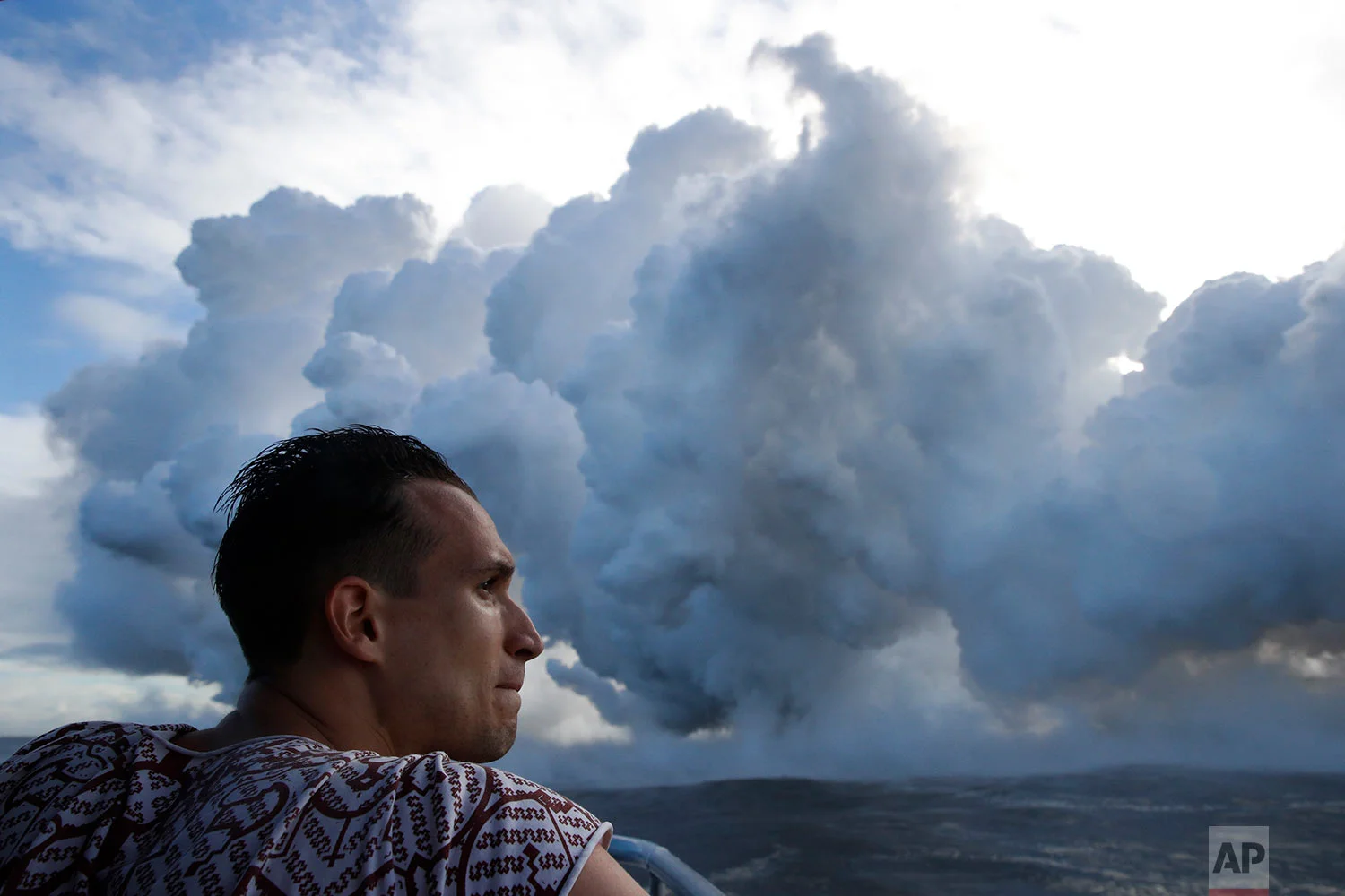 Gabor Kovacs, visiting from Hungary, watches as lava flows into the ocean, generating plumes of steam, near Pahoa, Hawaii, May 20, 2018. (AP Photo/Jae C. Hong)