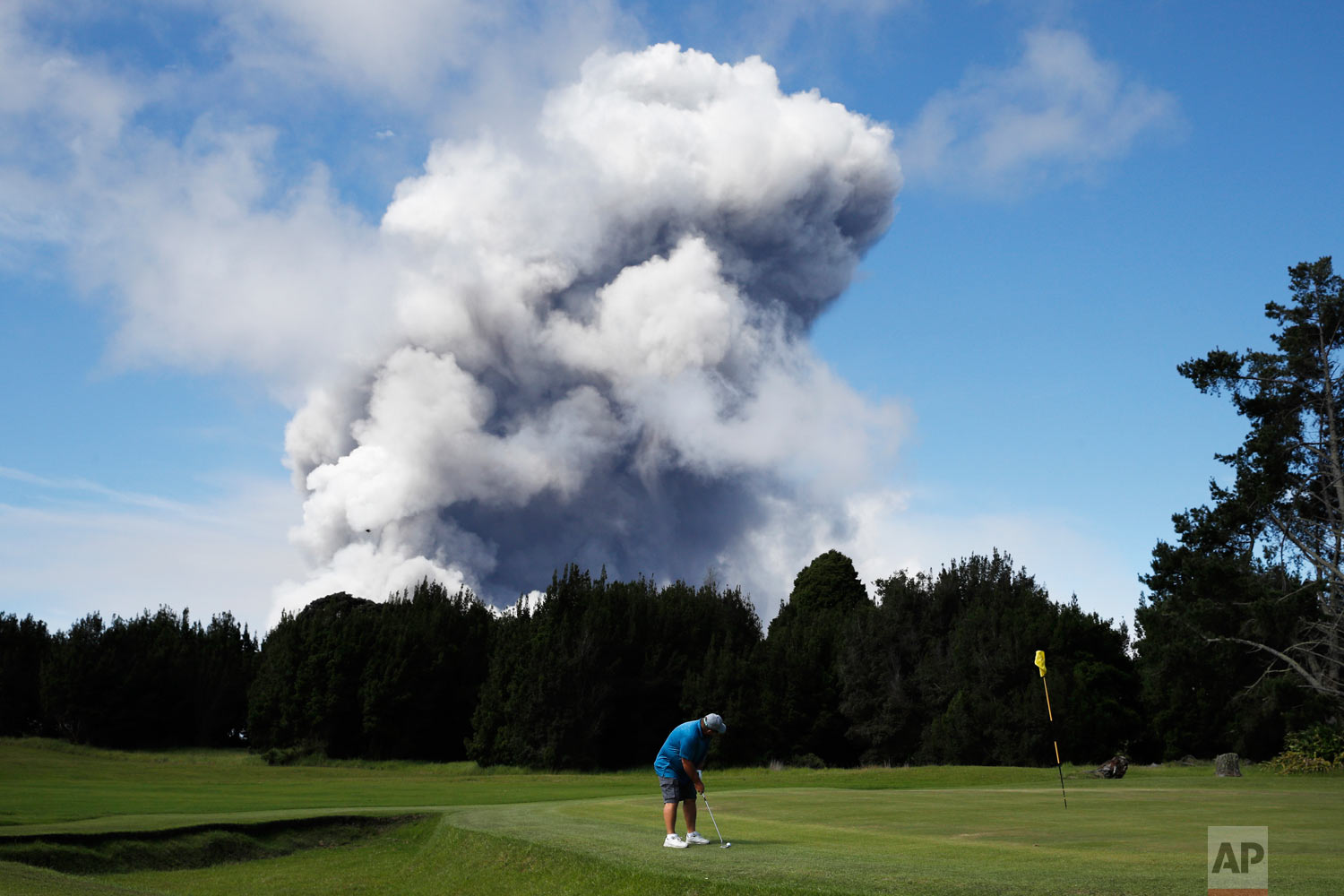  Doug Ralston plays golf in Volcano, Hawaii, as a huge ash plume rises from the summit of the Kiluaea volcano Monday, May 21, 2018. Lava from Hawaii's Kilauea volcano poured into the sea and set off a chemical reaction that created giant clouds of ac