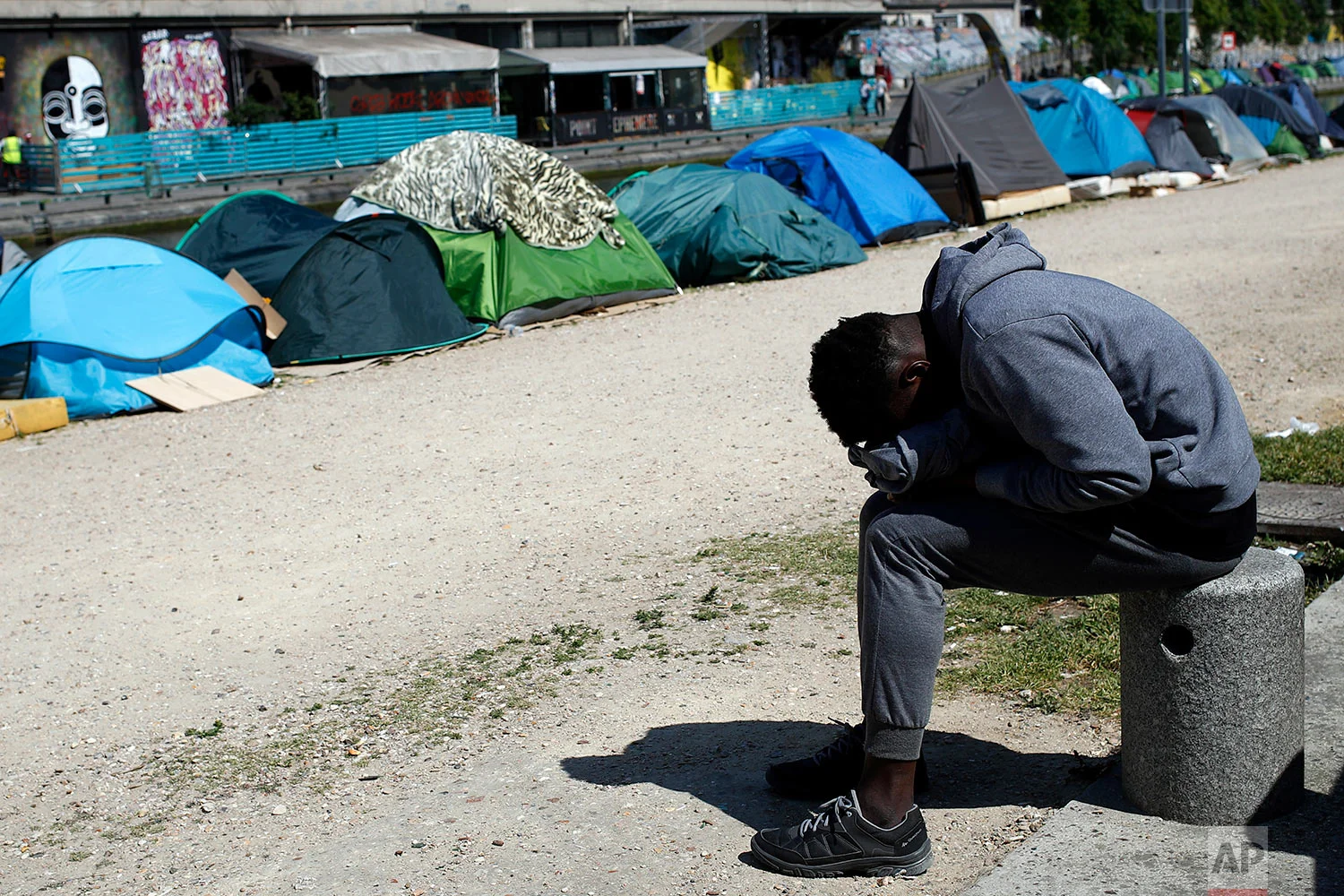 A migrant takes a nap near tents where asylum seekers have set up a makeshift camp alongside the Canal Saint-Martin, in Paris, Friday, May 18, 2018. (AP Photo/Francois Mori)
