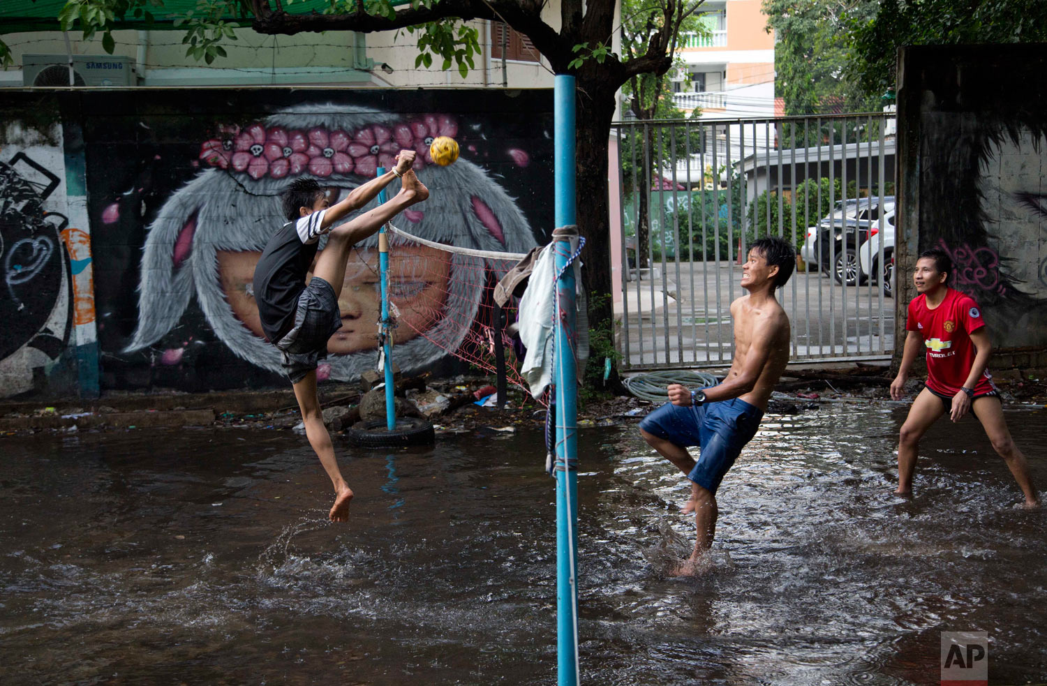 An airborne migrant worker kicks a rattan ball during a game of Chinlone in a field flooded by rain water in Bangkok, Thailand, Thursday, May 31, 2018. The popular Burmese sport Chinlone, a combination of sport and dance, is played between two teams consisting of six players each, passing a rattan ball back and forth with feet, knees and heads. (AP Photo/Gemunu Amarasinghe)
