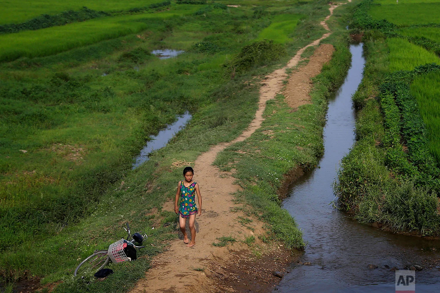A young girl dressed in her swimming suit walks along a stream between fields in Hamju, North Korea, on July 20, 2017. (AP Photo/Wong Maye-E)