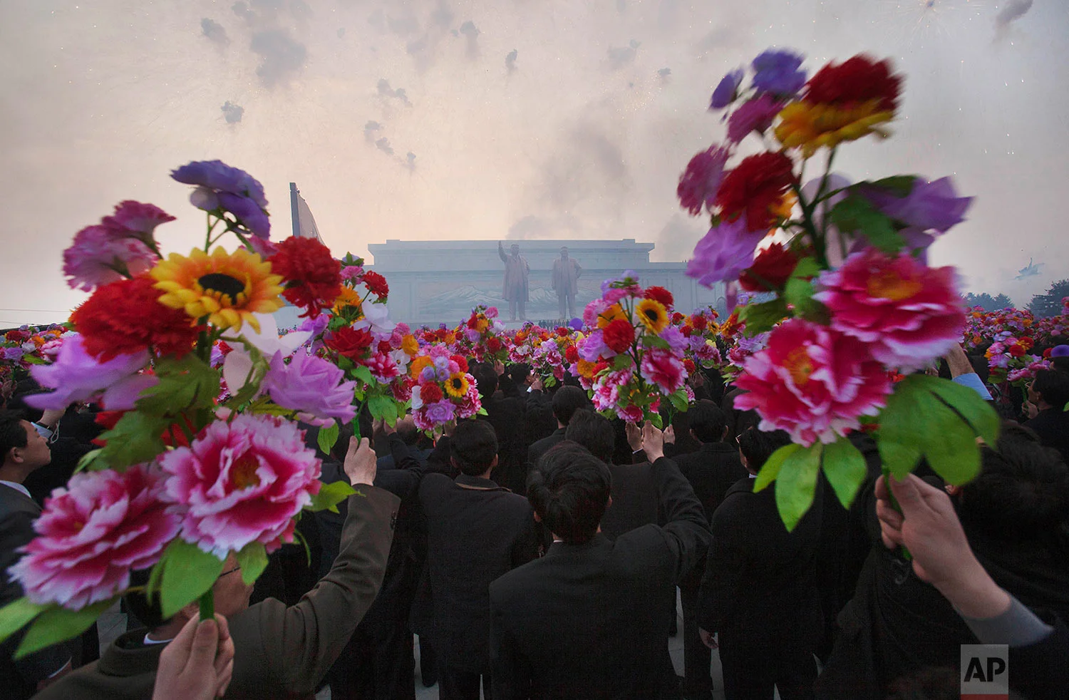North Koreans wave artificial flowers at an unveiling ceremony for statues of the late leaders Kim Il Sung and Kim Jong Il in Pyongyang, North Korea, on April 13, 2012. (AP Photo/David Guttenfelder)