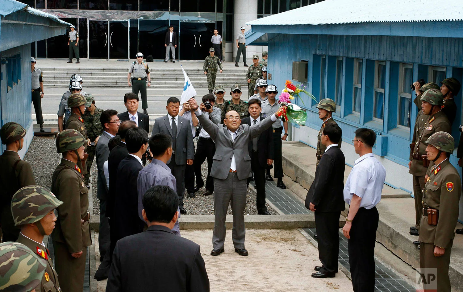 Activist No Su-hui, center, shouts "Long Live Reunification" in front of North Korean officials and soldiers, foreground, before crossing the demarcation line between North and South Korea where South Korean officials were waiting for him, at the Demilitarized Zone at Panmunjom, Korea, on July 5, 2012. South Korean officials immediately detained the activist for making an extended trip to Pyongyang without South Korean government approval as required by law. (AP Photo/Kim Kwang Hyon)