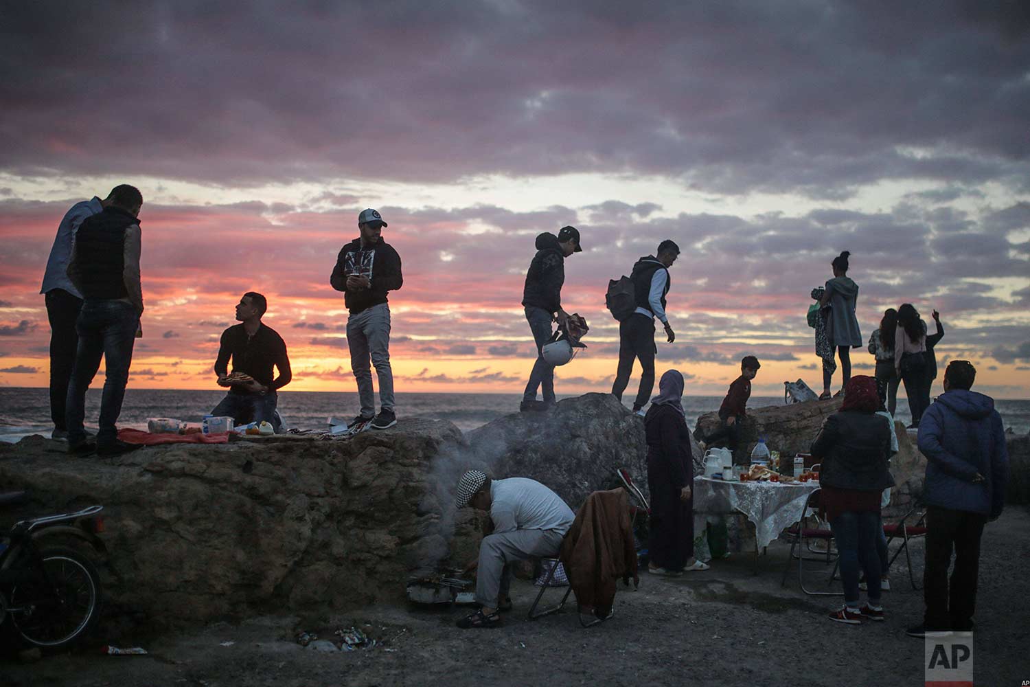  Beachgoers observe the sunset as a man grills meat for his family to break their fast in the holy month of Ramadan, Rabat, Morocco, Saturday, June 9, 2018. (AP Photo/Mosa'ab Elshamy) 