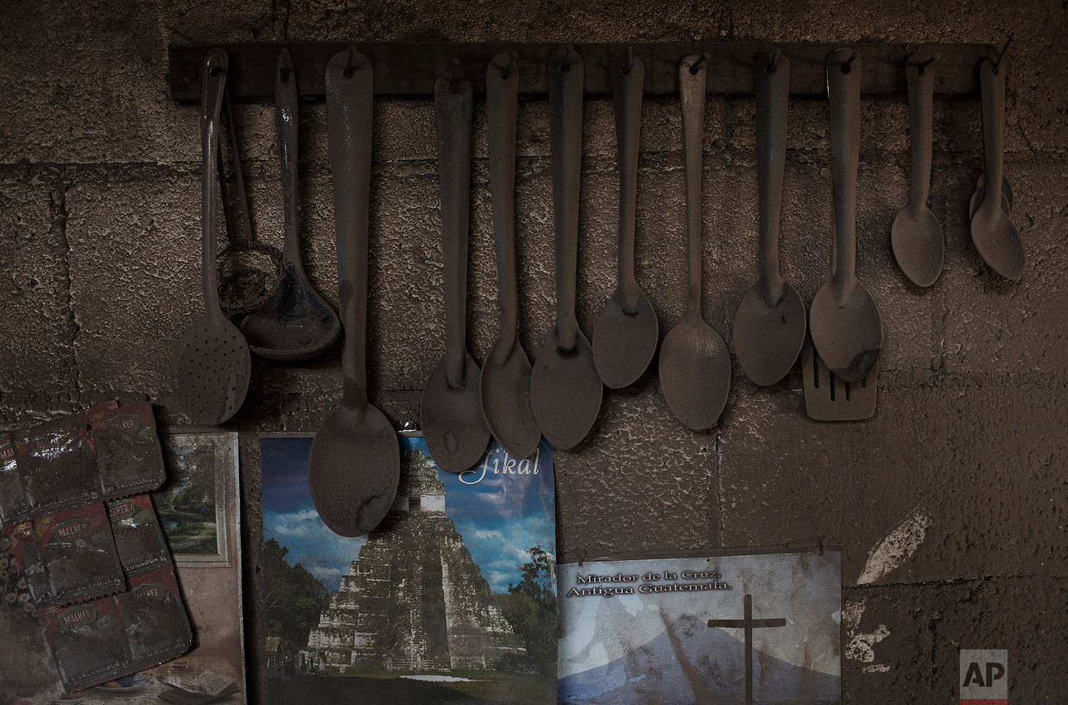  This June 9, 2018 photo shows kitchen utensils hanging above posters promoting the Mayan ruins Tikal and the Mirador de la Cruz, dusted with volcanic ash spewed by the Volcan de Fuego or Volcano of Fire, in San Miguel Los Lotes, Guatemala. (AP Photo