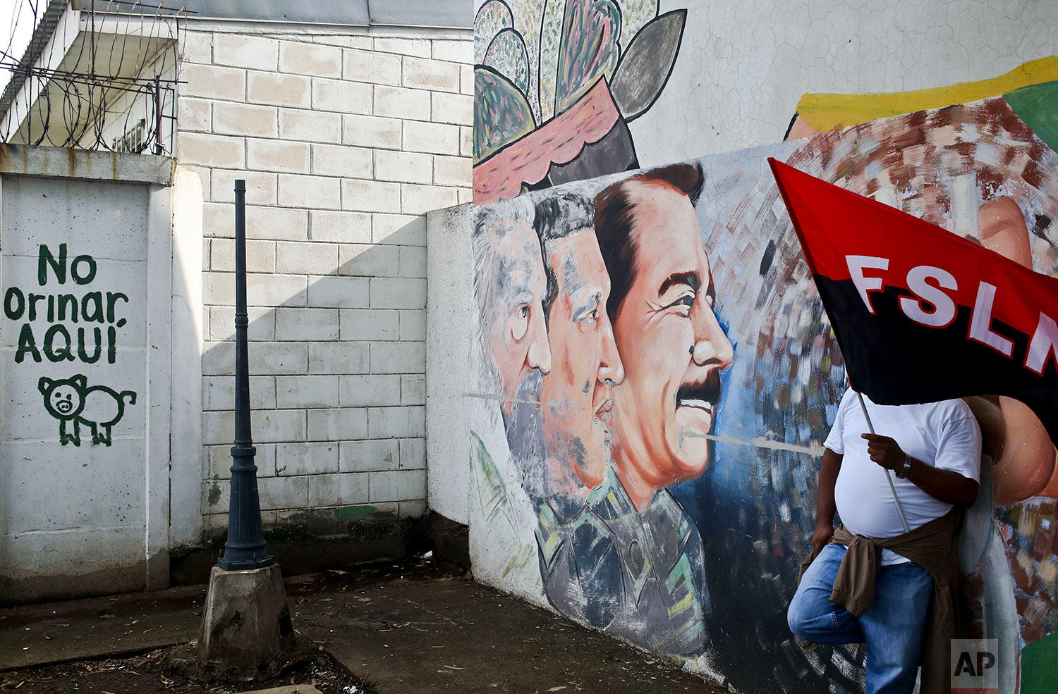  In this May 26, 2018 photo, a government supporter holds a Sandinista flag by a mural featuring Nicaragua's President Daniel Ortega, Venezuela's late President Hugo Chavez, and Cuba's late leader Fidel Castro, during government event in Managua, Nic