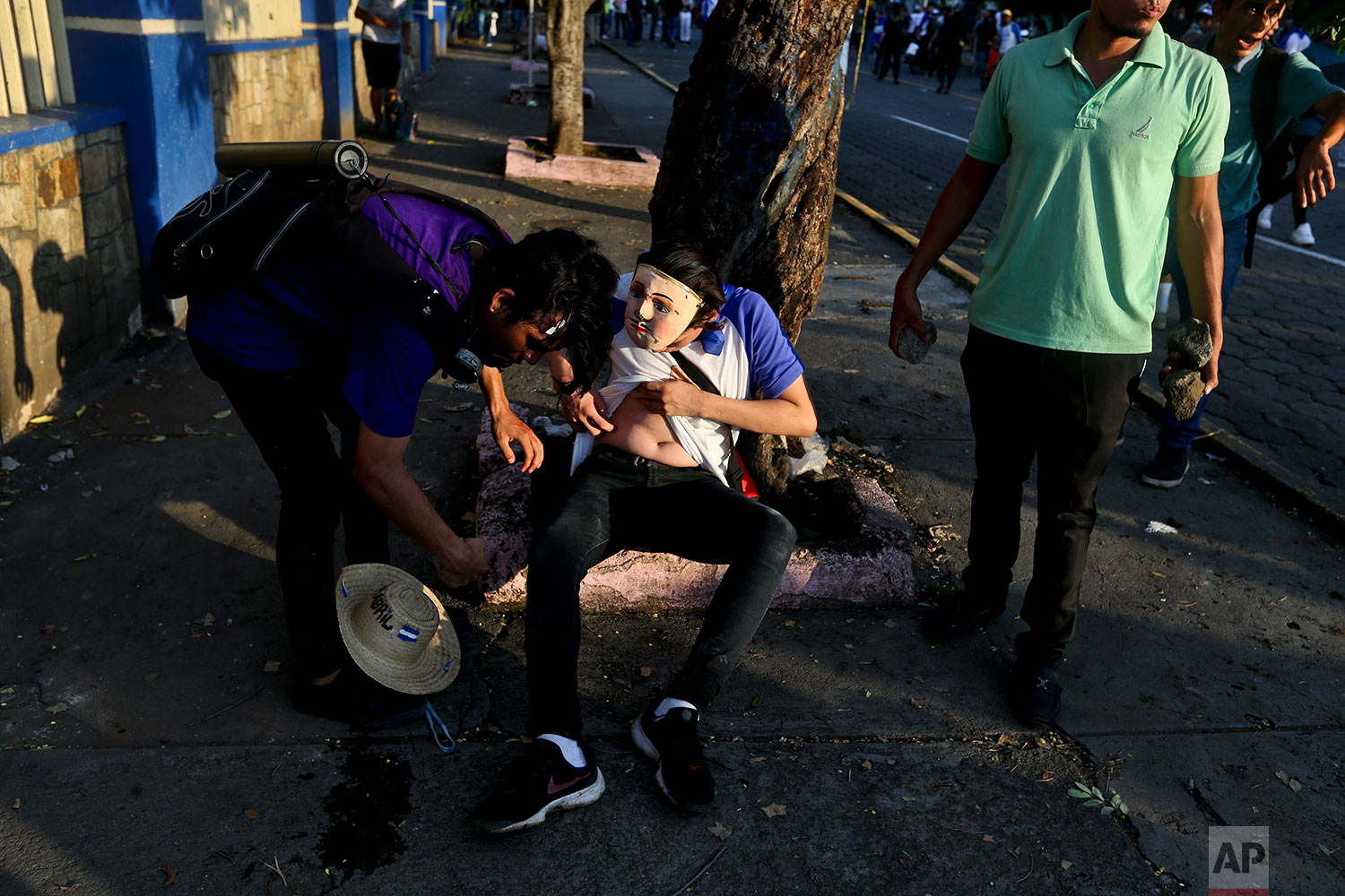  In this May 30, 2018 photo, a masked protester takes stock of his injury after  clashes with  police and government supporters in Managua, Nicaragua, during a march commemorating mother's day, and in honor mothers' children who have died during ongo