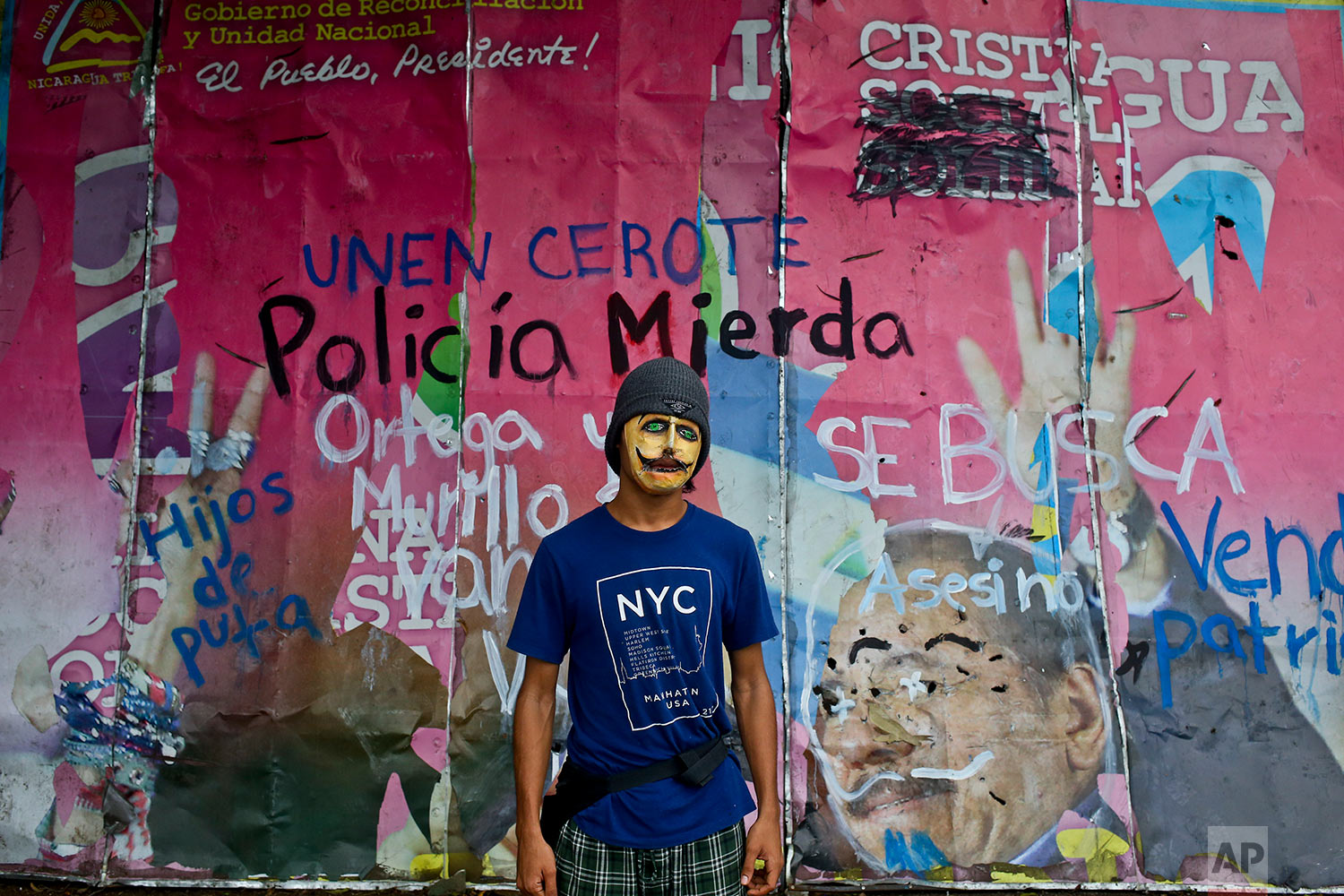  In this May 20, 2018 photo, a university student poses for a picture wearing a mask to hide his identity, in front a defaced billboard of Nicaragua¥s President Daniel Ortega and his wife, first lady Rosario Murillo, outside the Agrarian University i