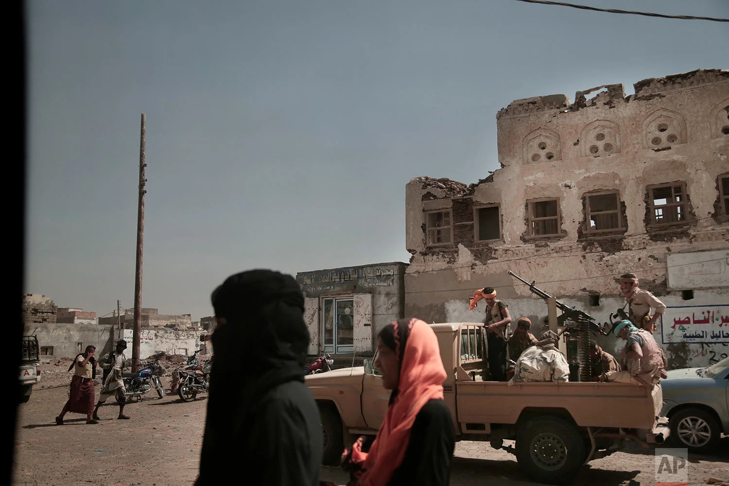 Women walk past Saudi-led coalition backed forces, leading the campaign to take over Hodeida, as they patrol Mocha, a port city on the Red Sea coast of Yemen. (AP Photo/Nariman El-Mofty)