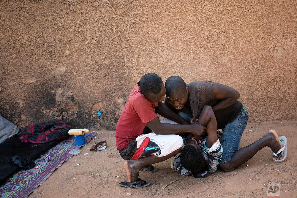  A young migrant who has been expelled from Algeria is restrained by others after he attempted to strip naked in a transit center in Arlit, Niger, on June 2, 2018. (AP Photo/Jerome Delay) 