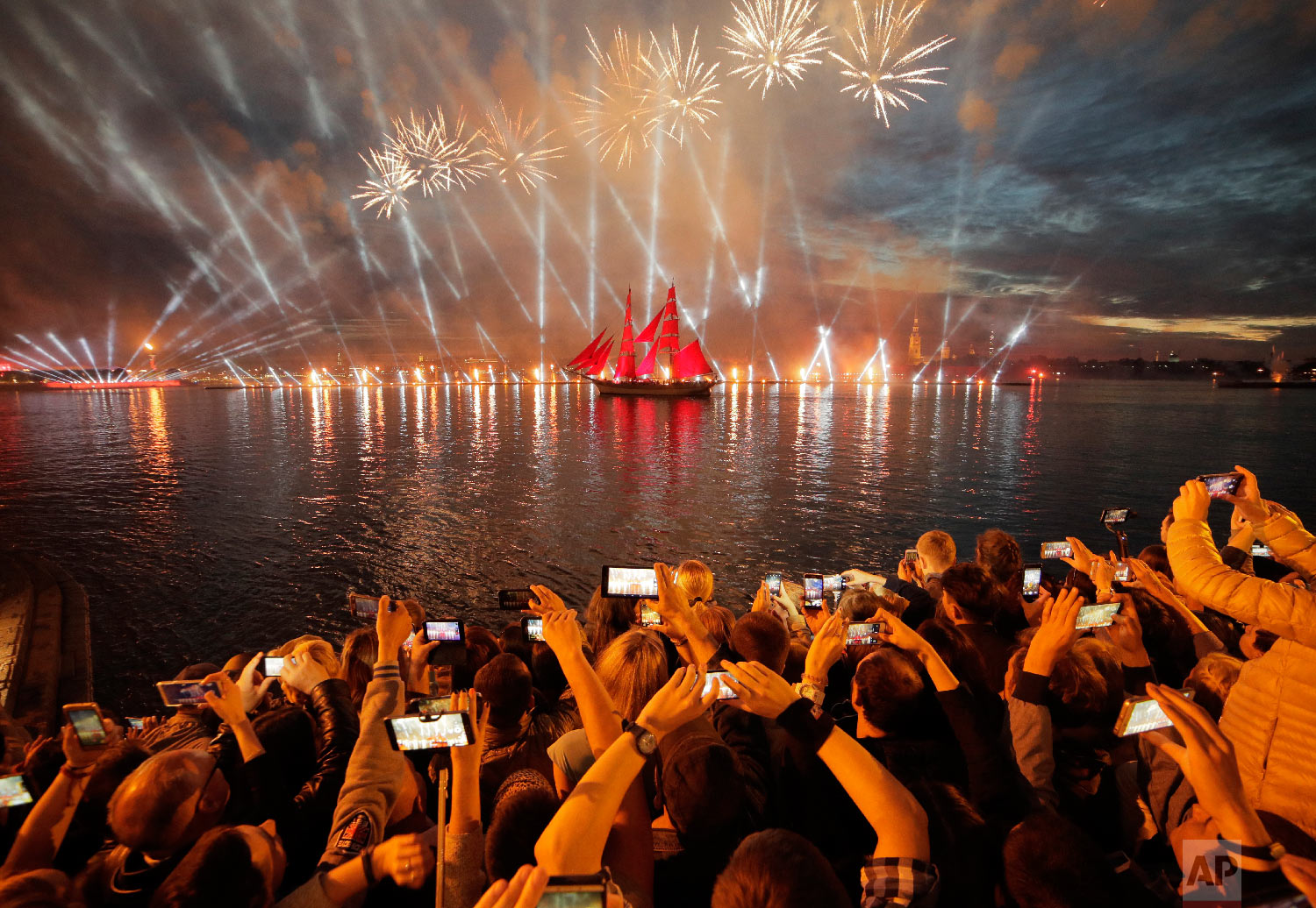 People watch fireworks and a brig with scarlet sails on the Neva River during the Scarlet Sails festivities marking school graduation in St.Petersburg, Russia on June 24, 2018. (AP Photo/Dmitri Lovetsky)