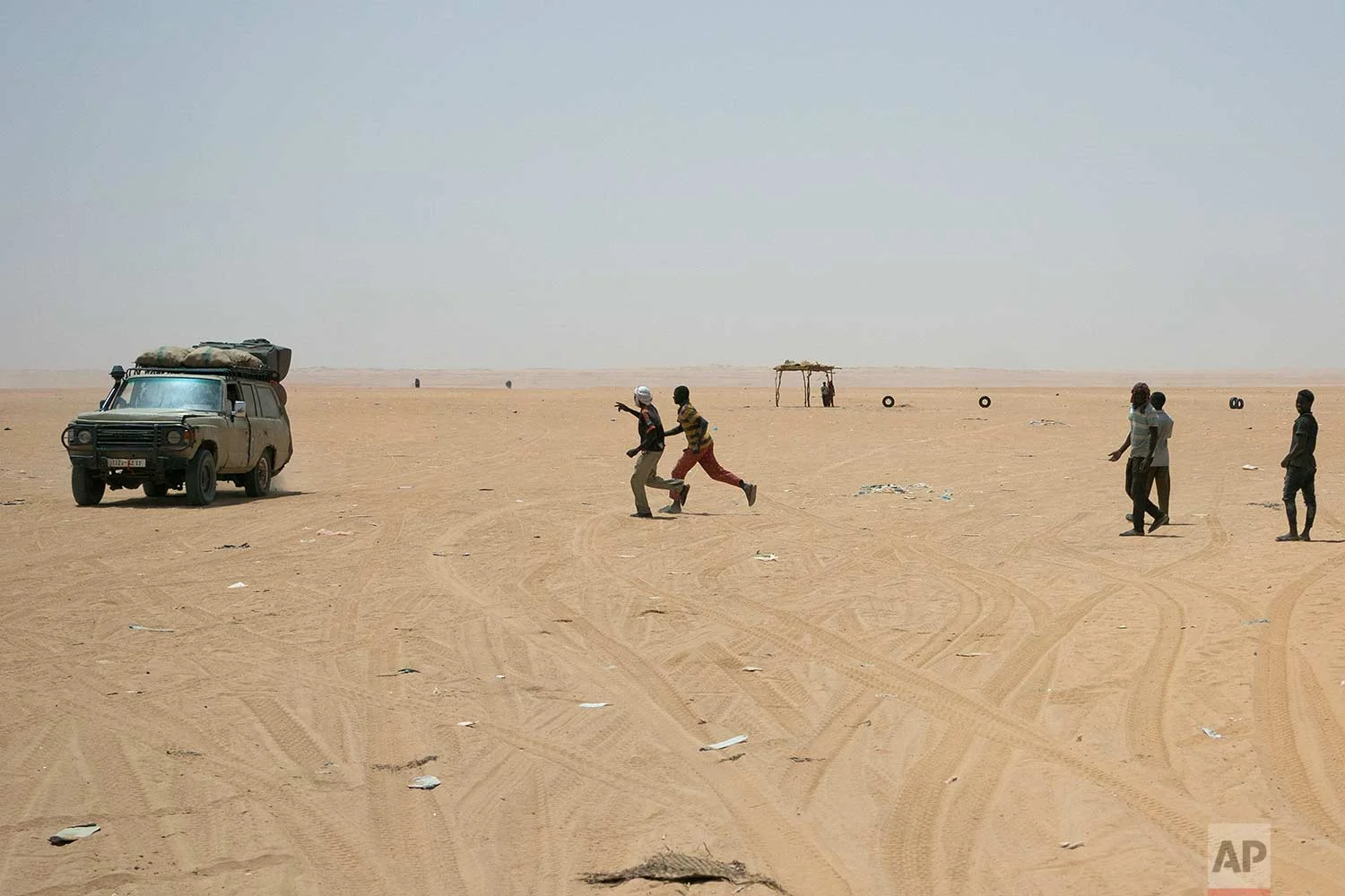 Migrants and locals wait for trucks arriving from Algeria to unload their cargo on Sunday, June 3, 2018, in order to earn money to pay for the trip north, at a giant desert trading post called "The Dune" in the no-man's land separating Niger and Algeria north of the Assamaka border post in northern Niger. (AP Photo/Jerome Delay)