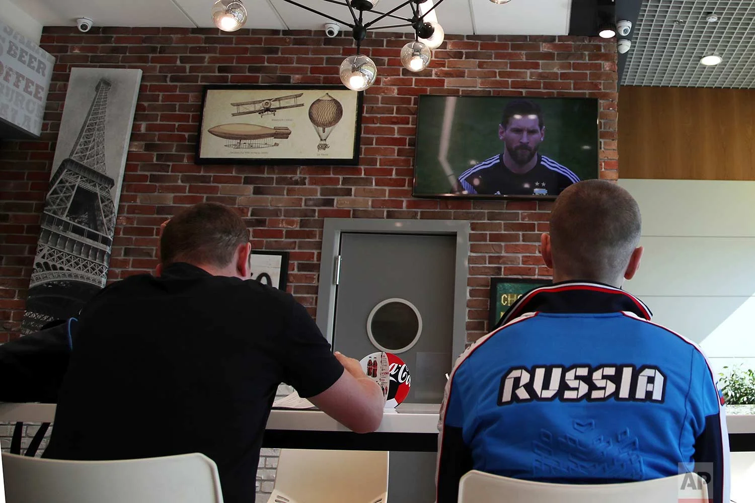 In this Saturday, June 16, 2018 photo, the TV shows the soccer star Lionel Messi during a match between Argentina and Iceland, as Russian fans watch the game, at Vnukovo International Airport, in Moscow, Russia. (AP Photo/Thanassis Stavrakis)
