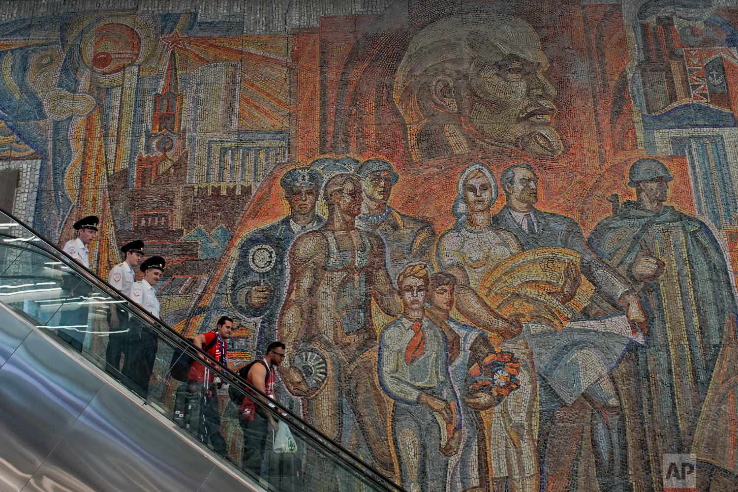  Soccer fans and police ride down an escalator at a subway station in front of a large soviet-era mural depicting Soviet founder Vladimir Lenin, top, during the 2018 soccer World Cup in Nizhny Novgorod, Russia on June 25, 2018. (AP Photo/Victor R. Ca