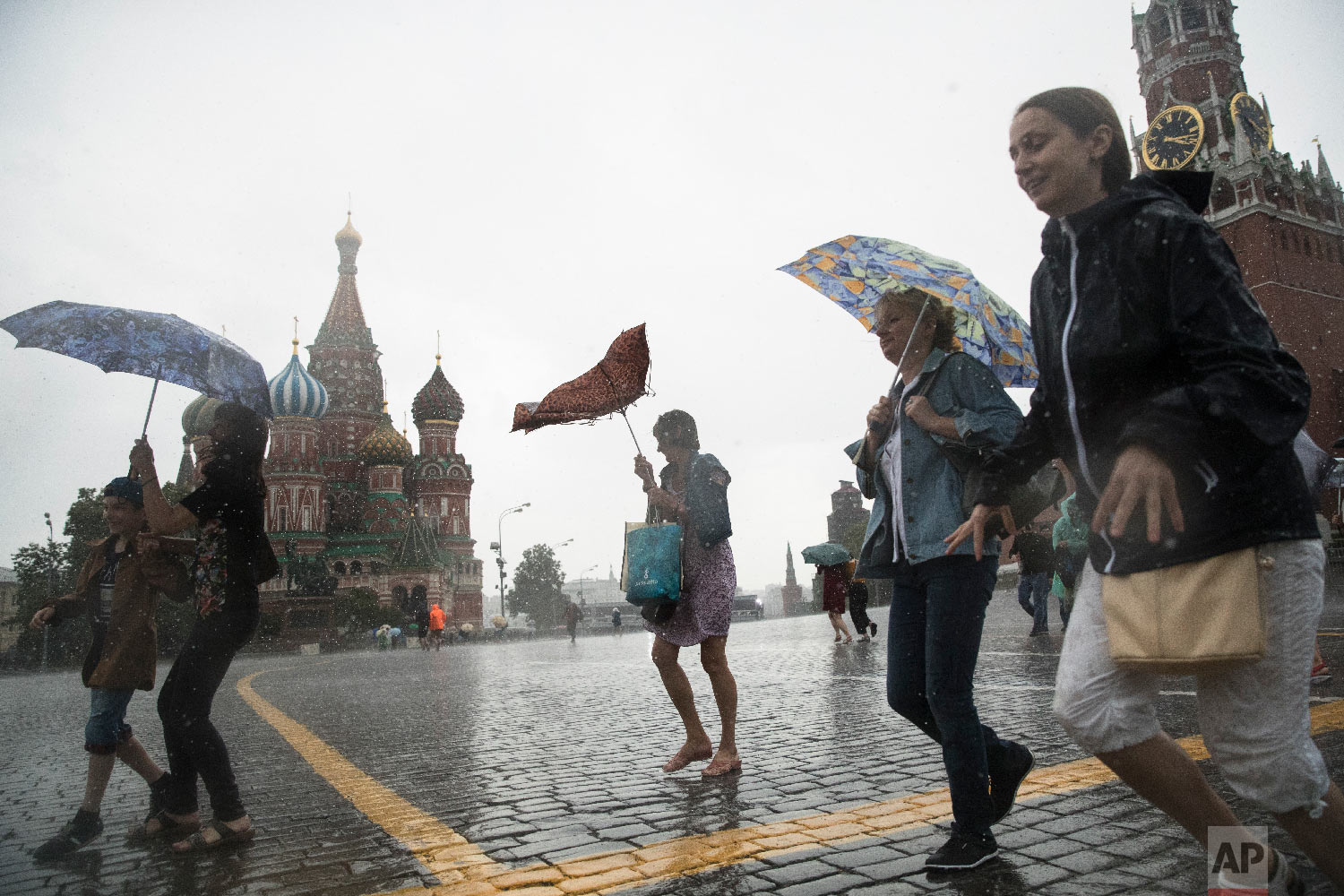  Tourists take cover from a heavy rain under umbrellas in Red Square with the with St. Basil's Cathedral, left, and the Spasskaya Tower, right, in the background, in Moscow, Russia on June 30, 2018. (AP Photo/Pavel Golovkin) 