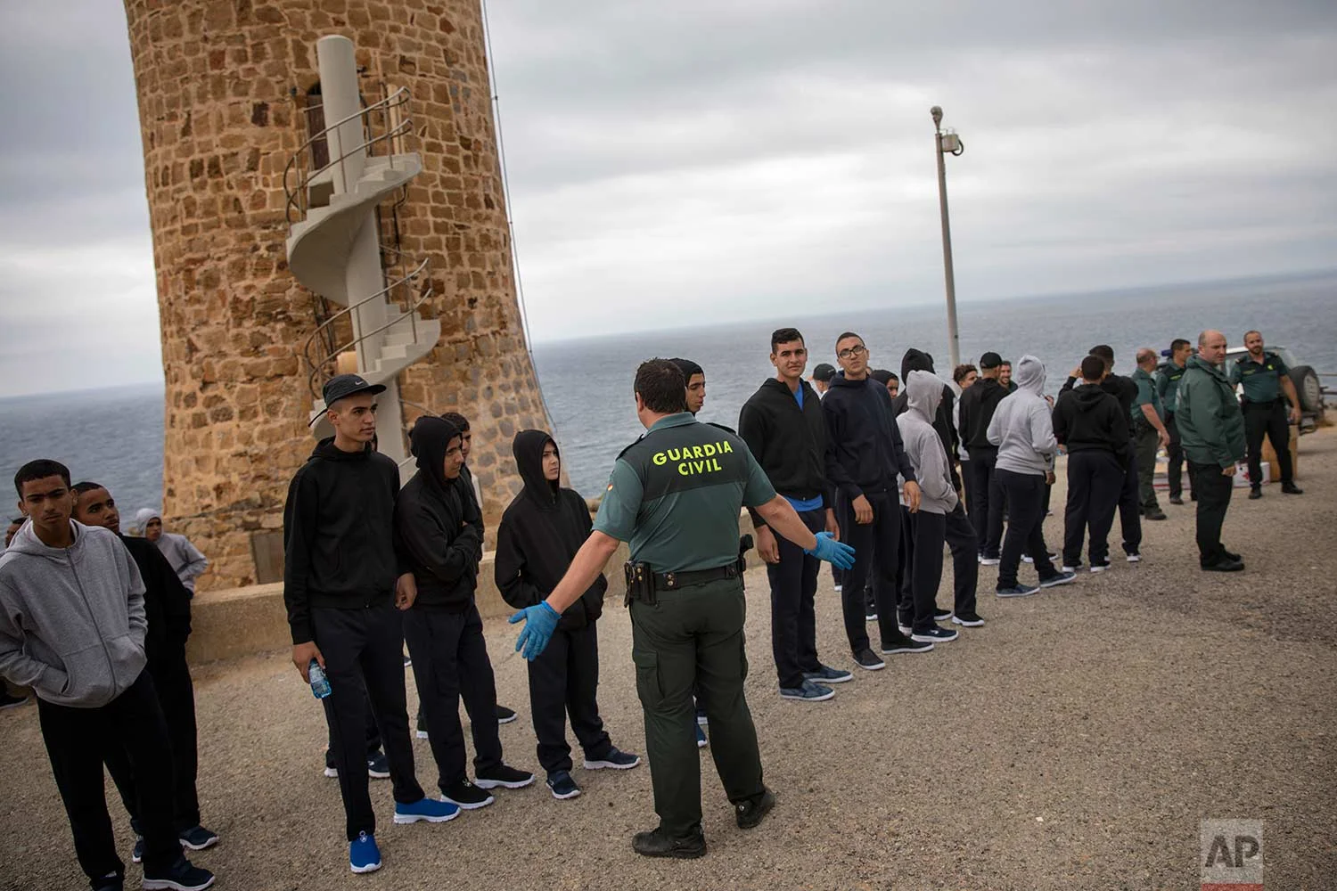 A Guardia Civil officer stands next to Moroccan migrants as they line up by the Camarinal Lighthouse after arriving on the beach by sailing in a rubber dinghy near Tarifa, in the south of Spain, Thursday, June 28, 2018. The group consisted of 35 unaccompanied Moroccan migrants. (AP Photo/Emilio Morenatti)