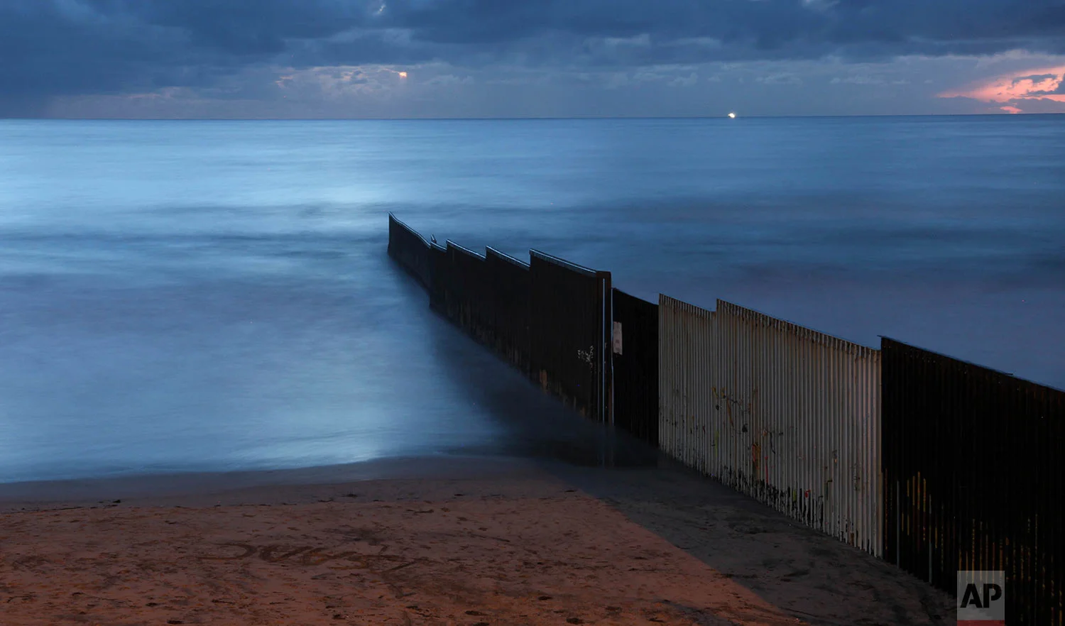In this Feb. 28, 2018 photo published in June, the sun sets over the U.S.-Mexico barrier that runs into the Pacific Ocean, seen from Tijuana, Mexico. (AP Photo/Emilio Espejel)