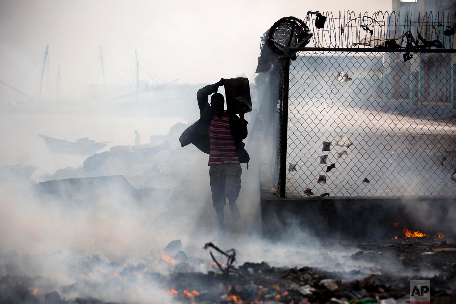  A man carries a container of sea water past burning trash at the harbor in Port-au-Prince, Haiti, June 7, 2018, to keep the fire from burning his merchandise. (AP Photo/Dieu Nalio Chery) 