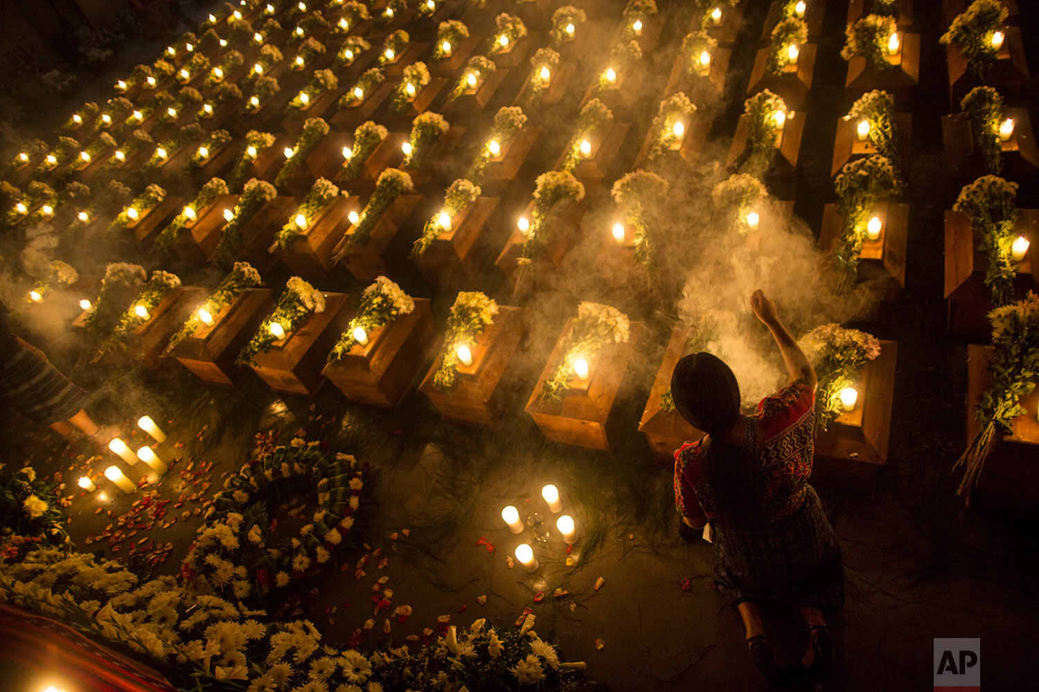  In this June 20, 2018 photo, a woman spreads incense over the coffins holding the remains of 172 unidentified people who were discovered buried at what once was a military camp in San Juan Comalapa, Guatemala, one day before their formal burial at t