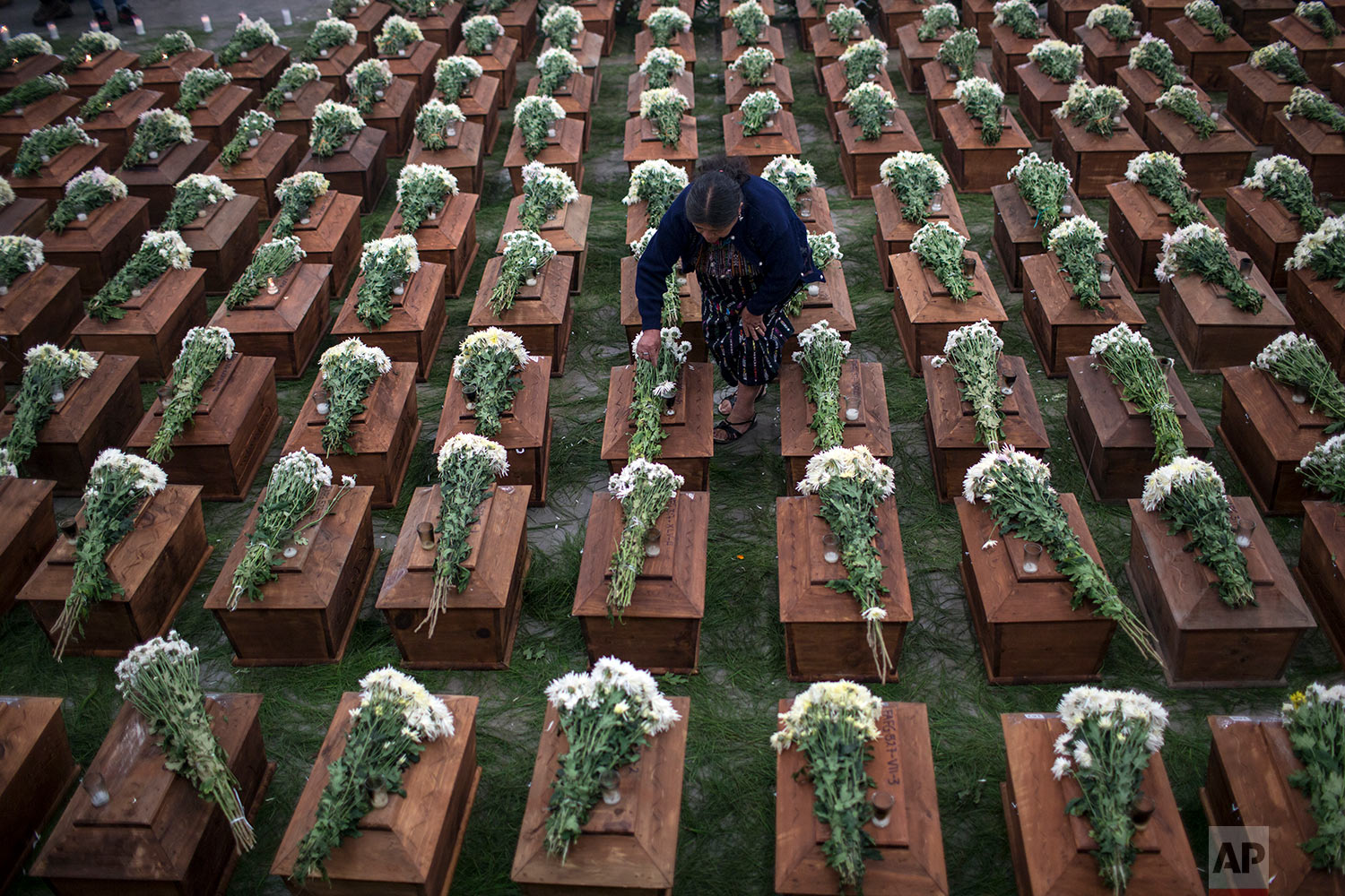  In this June 20, 2018 photo, a woman places flowers on coffins holding the remains of 172 unidentified people who were exhumed from what was once a military camp, during a funeral ceremony in San Juan Comalapa, Guatemala, one day before their proper