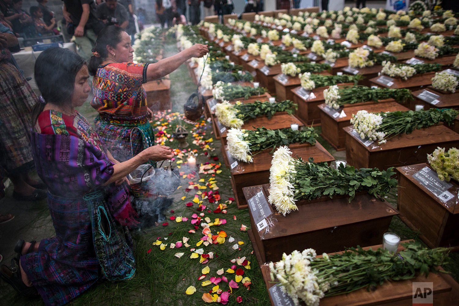  In this June 20, 2018 photo, women burn incense over the remains of 172 unidentified people, who were exhumed from what was once a military camp, during a funeral ceremony in San Juan Comalapa, Guatemala, one day before the formal burial. (AP Photo/