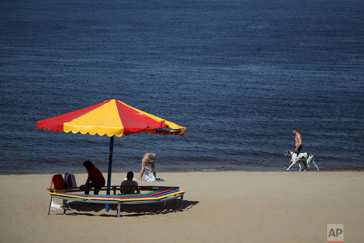 A man walks with his dog as people spend a sunny day on a riverfront beach, during the 2018 soccer World Cup in Samara, Russia on Tuesday, June 3, 2018. (AP Photo/Thanassis Stavrakis)