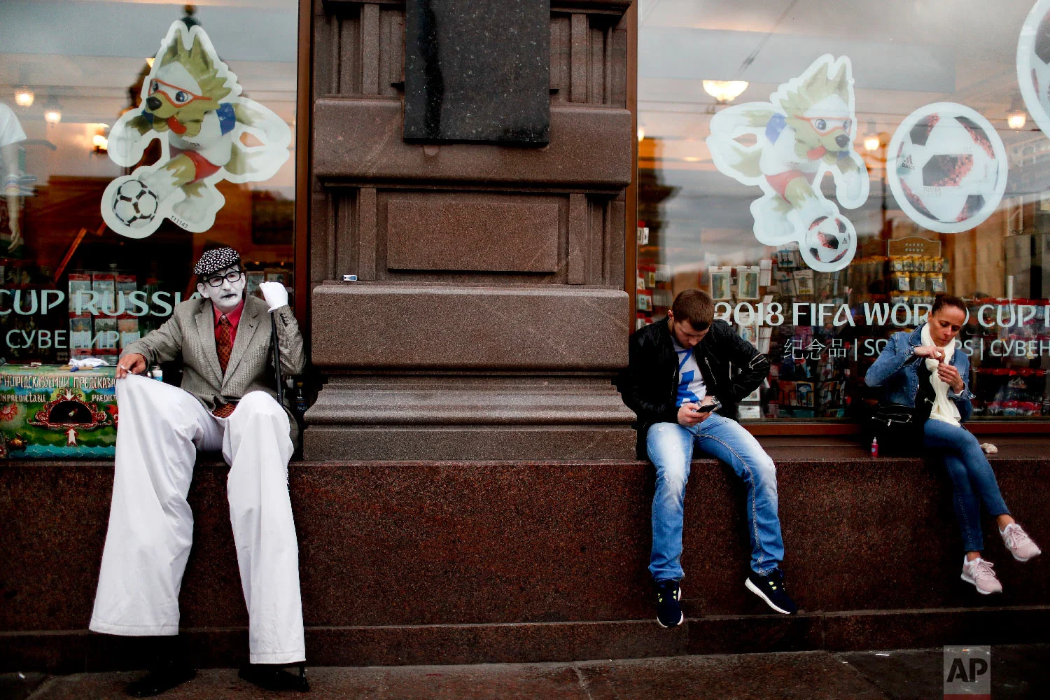 Residents and a street artist sit in a window shop during the 2018 soccer World Cup in St. Petersburg, Russia on Sunday, July 8, 2018. (AP Photo/Natacha Pisarenko)