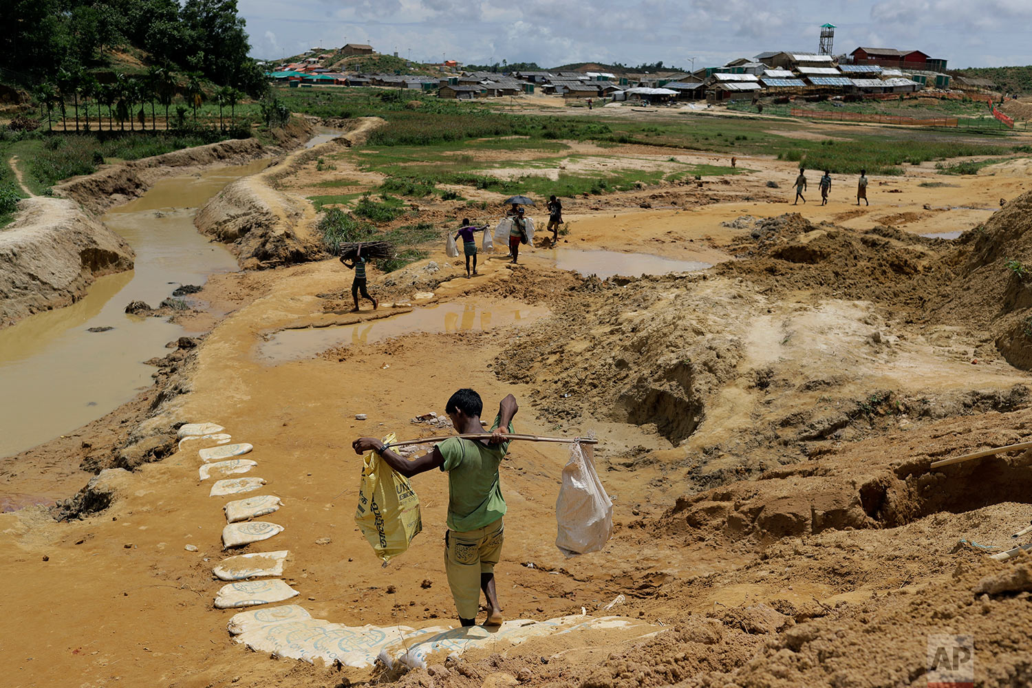  In this Thursday, June 28, 2018, photo, Rohingya refugees carry construction material to an extended area of Kutupalong refugee camp in Bangladesh where some refugees living in areas considered at risk of landslides and flooding were relocated to. (