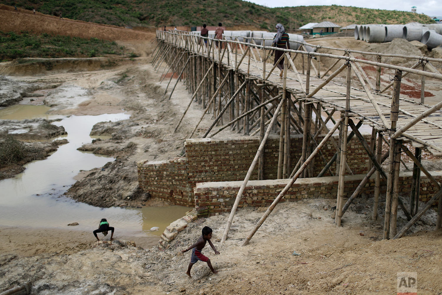  In this Thursday, June 28, 2018, photo, Rohingya refugees cross a newly built bridge in the extended area of Kutupalong refugee camp in Bangladesh where some refugees living in areas considered at risk of landslides and flooding were relocated to. (