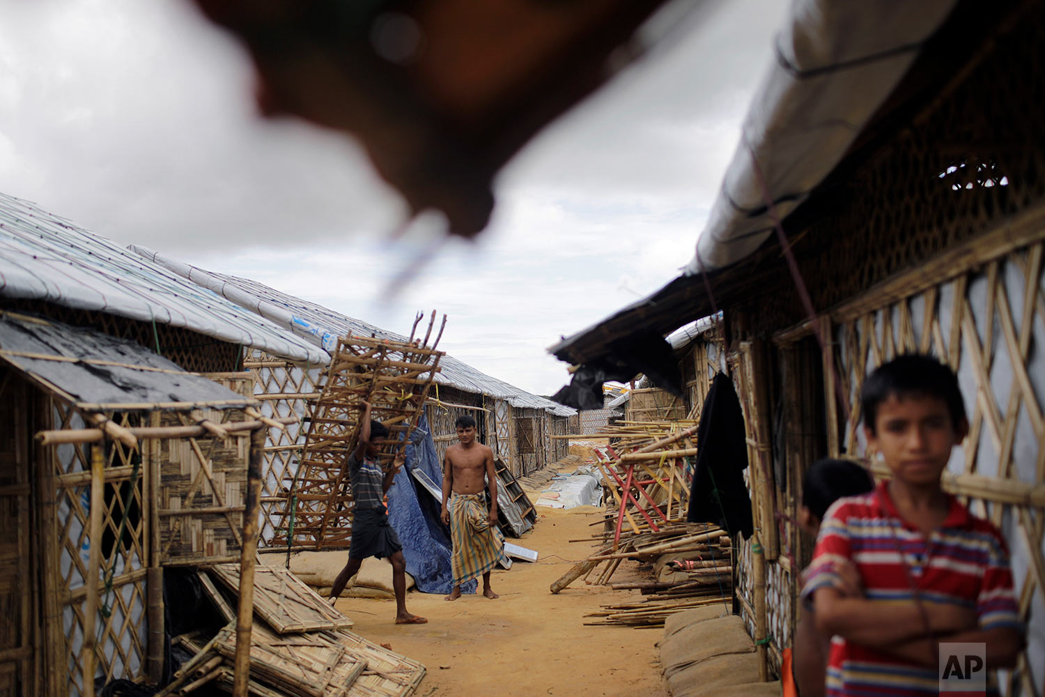 In this Thursday, June 28, 2018, photo, Rohingya refugees carry construction material through huts built in an extended area of Kutupalong refugee camp in Bangladesh where some refugees living in areas considered at risk of landslides and flooding w