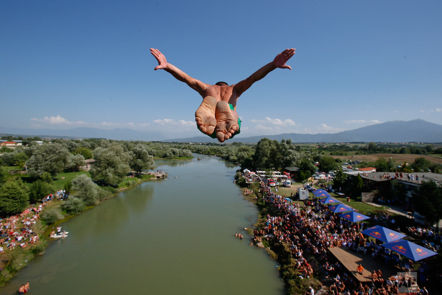 Spectators watch from the river banks as a diver launches from the Ura e Shejnt bridge during the 68th annual high diving competition, near the town of Gjakova, Kosovo on Sunday, July 22, 2018. (AP Photo/Visar Kryeziu)