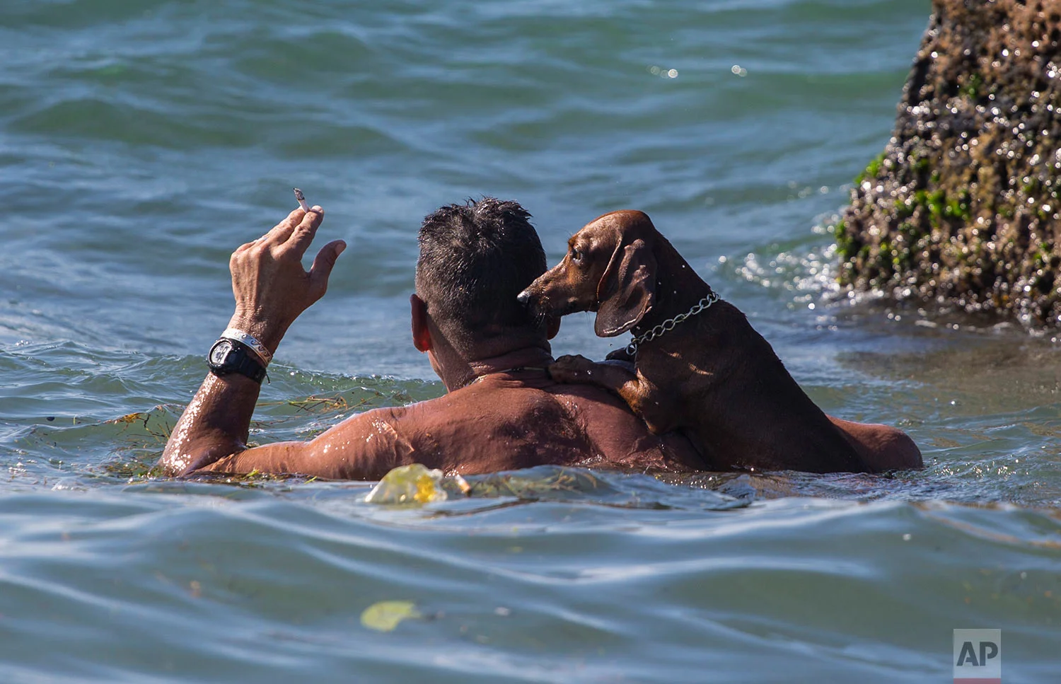 A man holds his cigarette above the ocean waterline as he takes a dip with his dog near Playita 16 in Havana, Cuba, July 22, 2018. (AP Photo/Desmond Boylan)