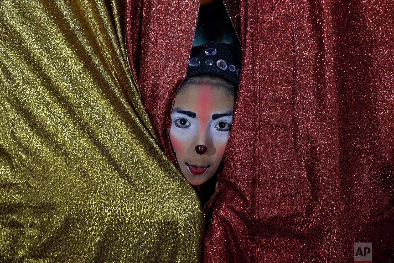 Joshep Balta, who plays the part of a clown named "Cachupito," peers through the tent curtain to see how many people are waiting for the show, put on by the International Circus, set up in the shanty town of Puente Piedra on the outskirts of Lima, Peru, July 20, 2018. Balta, a 12-year old clown whose parents work at the circus setting up and breaking down the encampment, was discovered by the circus two years ago when he was performing as a clown at street corners. (AP Photo/Martin Mejia)