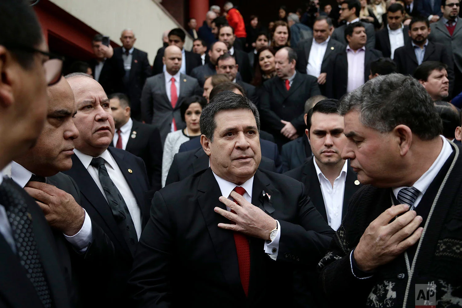 Paraguay's President Horacio Cartes straightens his tie as he waits for the arrival of the coffin of his Agriculture Minister Luis Gneiting, for a memorial service at the Colorado Party headquarters in Asuncion, Paraguay, July 27, 2018. The minister and three other people died when the twin-engine plane they were traveling in went down in a marshy area shortly after taking off at night from an airport. (AP Photo/Jorge Saenz)