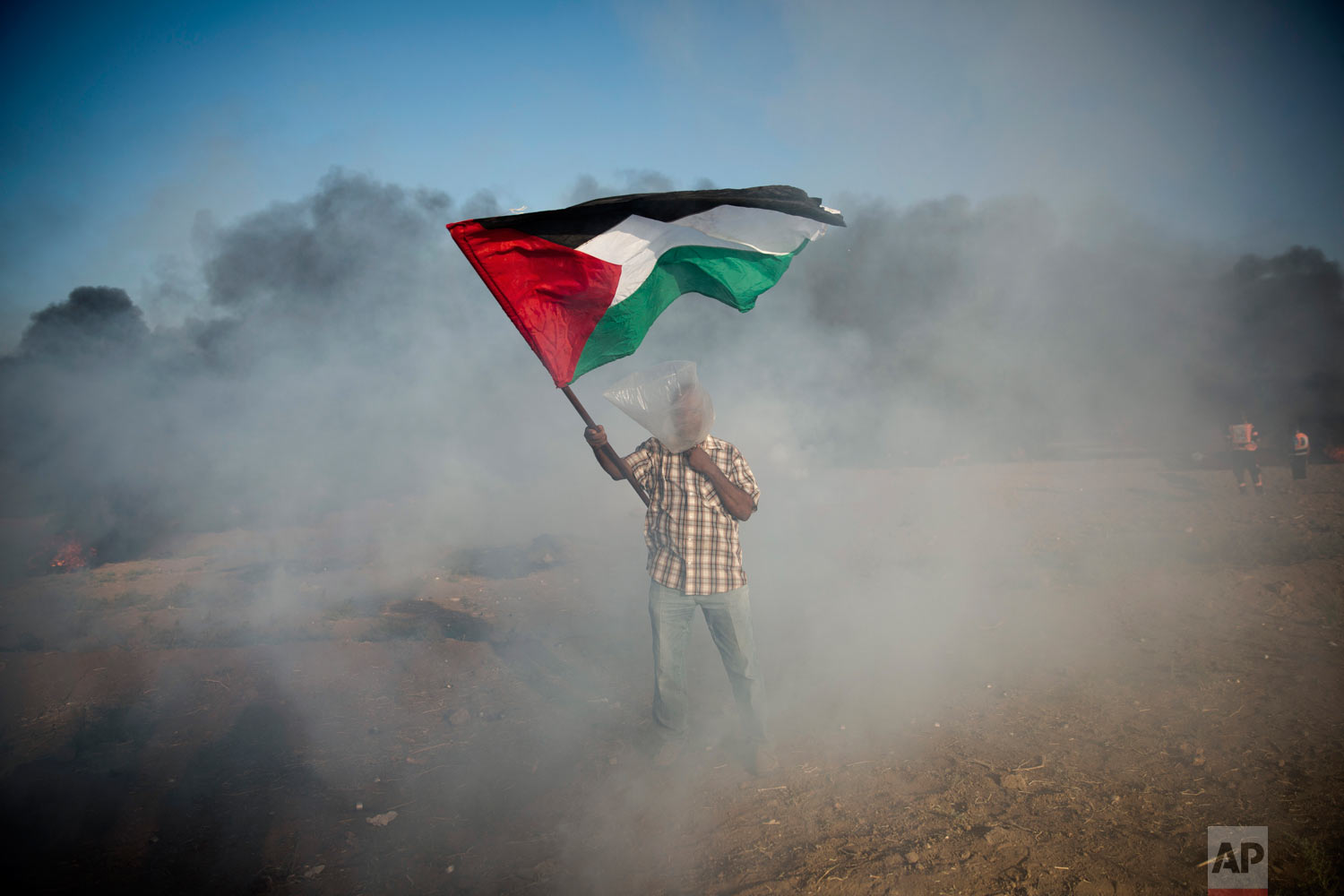  A Palestinian protester wears a plastic bag on his head as a protection from teargas as he waves a national flag during a protest at the Gaza Strip's border with Israel, Friday, Aug.10, 2018. Violence erupted at the Gaza border Friday after the terr