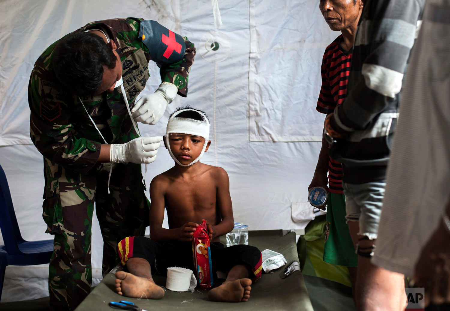A military paramedic tends to a boy who's head was injured from Sunday's earthquake at a makeshift hospital in Kayangan, Lombok Island, Indonesia, Wednesday, Aug. 8, 2018. The north of Lombok has been devastated by the magnitude 7.0 quake that struck Sunday night, damaging thousands of buildings and killing dozens. (AP Photo/Fauzy Chaniago)