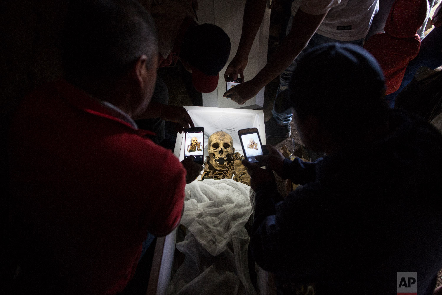  In this Aug. 14, 2018 photo, relatives take cell phone pictures of the remains of Fortunate Ventura Huamacusi, a man who was killed by the Peruvian army in 1983, before placing the coffin in its niche at the Rosaspata cemetery in Peru's Ayacucho pro