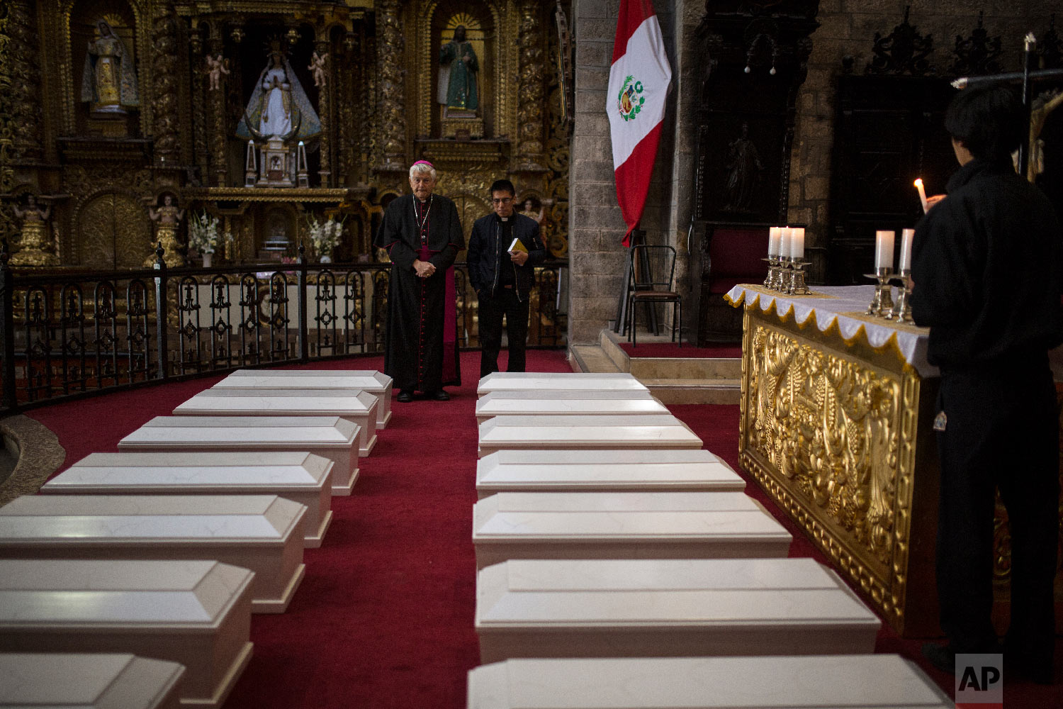  In this Aug. 14, 2018 photo, Ayacucho's Bishop Salvador Jose Miguel Pineiro, left, stands with an assistant behind the coffins of villagers who were killed by Shining Path guerrillas and the Peruvian army in the 1980s, inside the Cathedral in Ayacuc