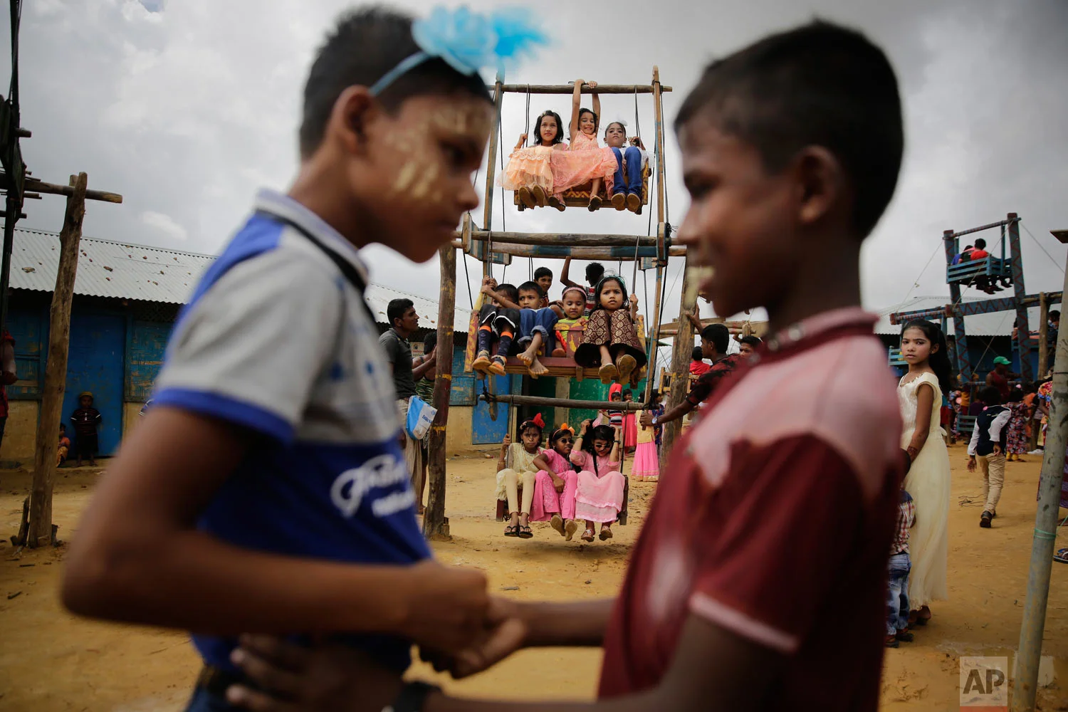 Rohingya refugee boys greet each other as girls ride in a ferris wheel, specially brought in to the camps for Eid al Adha celebrations at the Kutupalong refugee camp, Bangladesh, Wednesday, Aug. 22, 2018. Hundreds of thousands of Rohingya refugees are celebrating Eid al-Adha in sprawling Bangladeshi camps where they have been living amid uncertainty over their future after they fled Myanmar to escape violence and a massive crackdown. (AP Photo/Altaf Qadri)